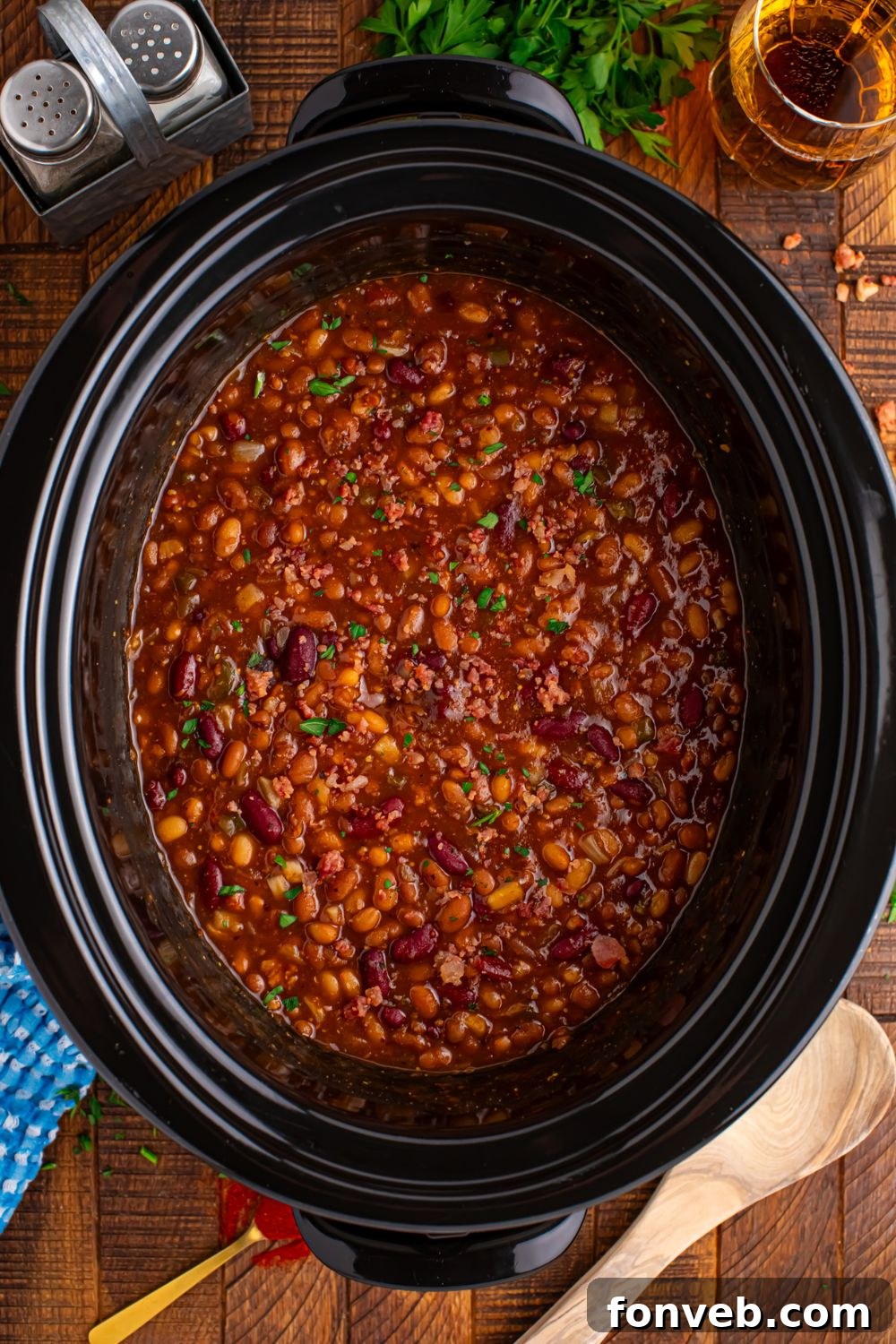 Crockpot bourbon baked beans in crockpot on table with wooden table and garnishes on table 