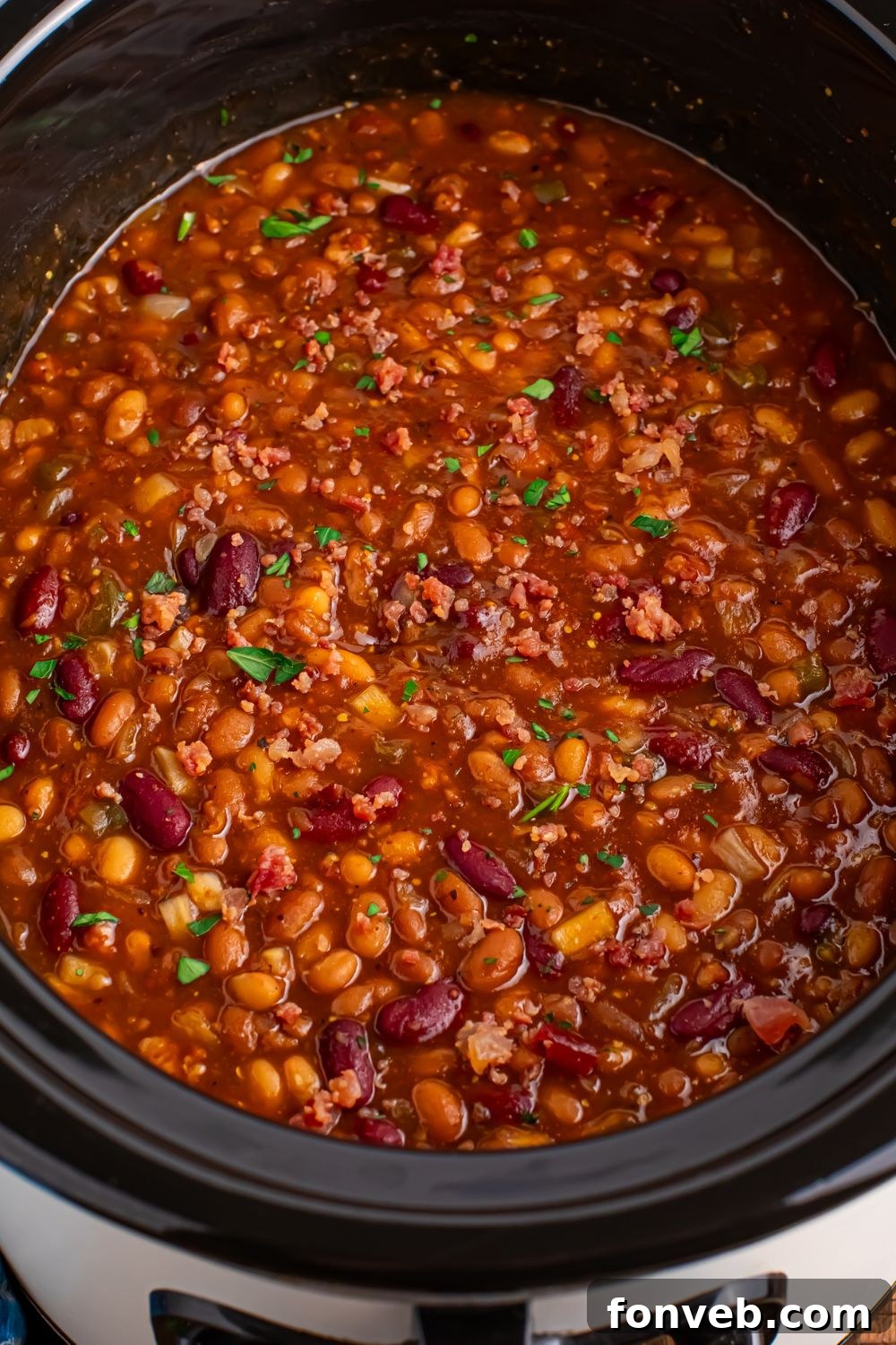 Crockpot bourbon baked beans in a crockpot with a sprinkle of parsley on top 