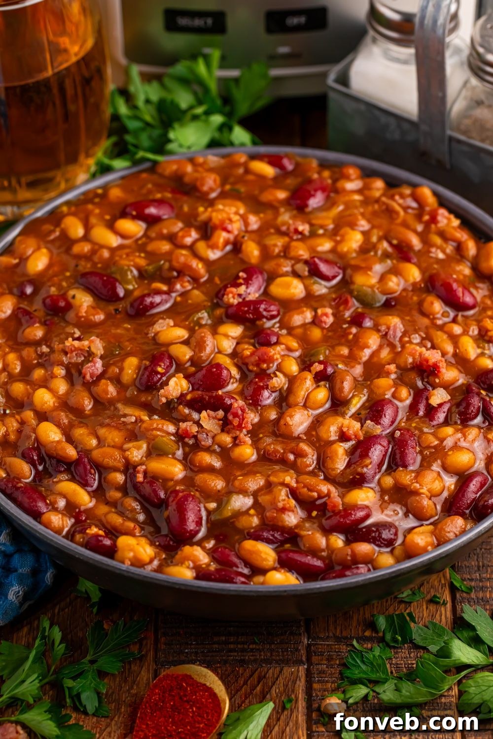 Crockpot Bourbon Brown Sugar Baked Beans in a bowl sitting on table with some fresh herbs to side of bowl