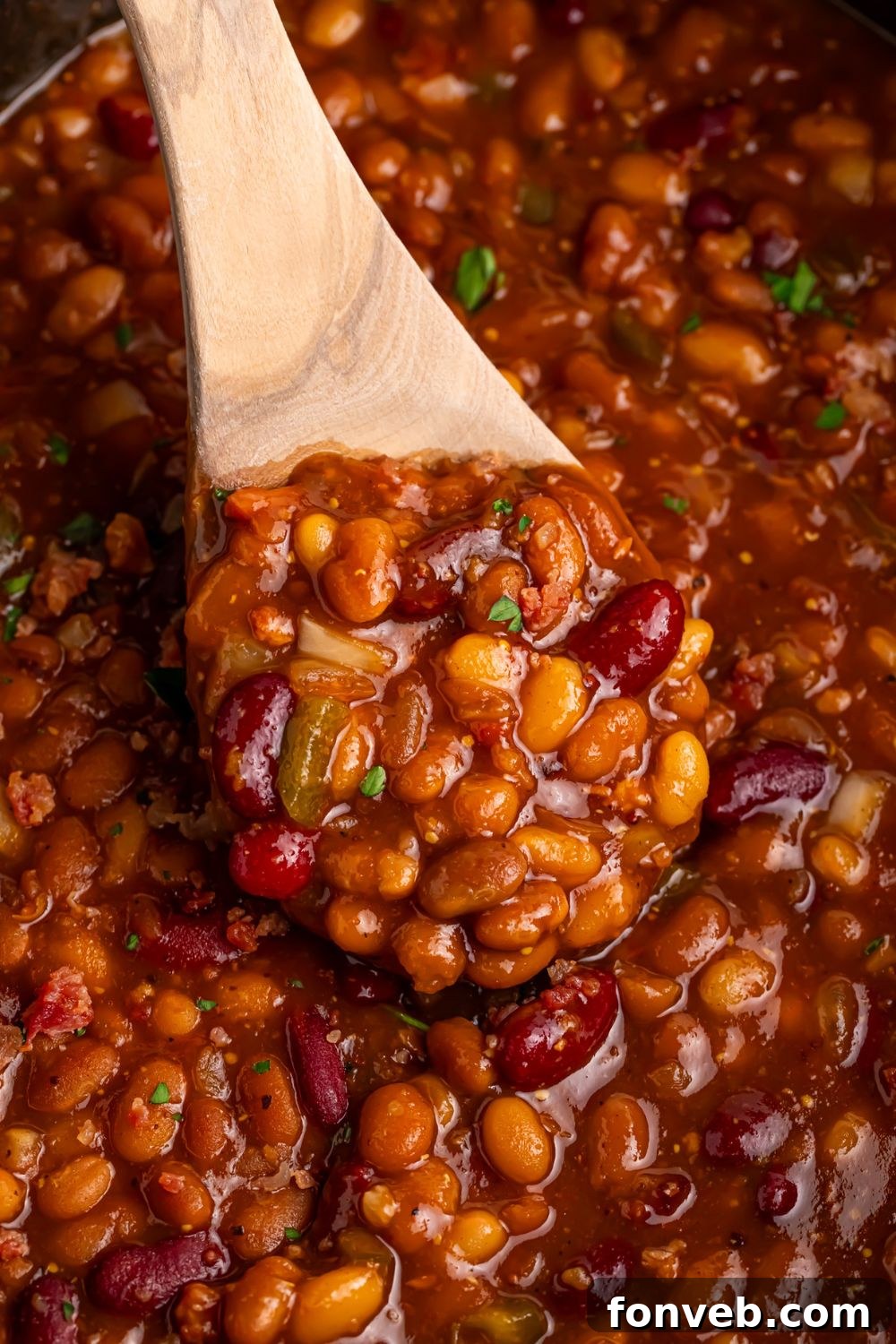 Crockpot Bourbon Brown Sugar Baked Bean in CrockPot with a wooden spoon scooping some out of container 