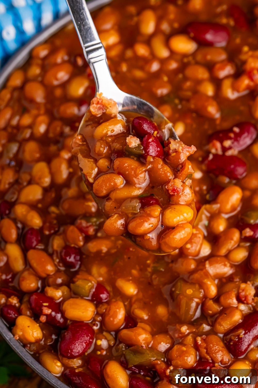 Crockpot bourbon baked beans in a bowl with a spoon scooping some out of bowl 