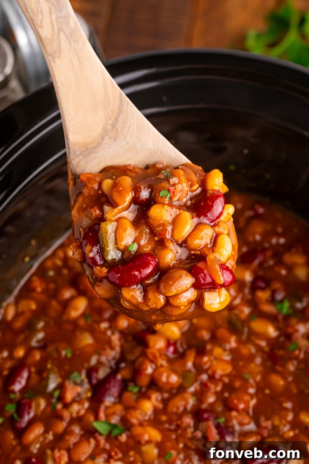 Crockpot bourbon baked beans on a wooden spoon above crockpot on table 