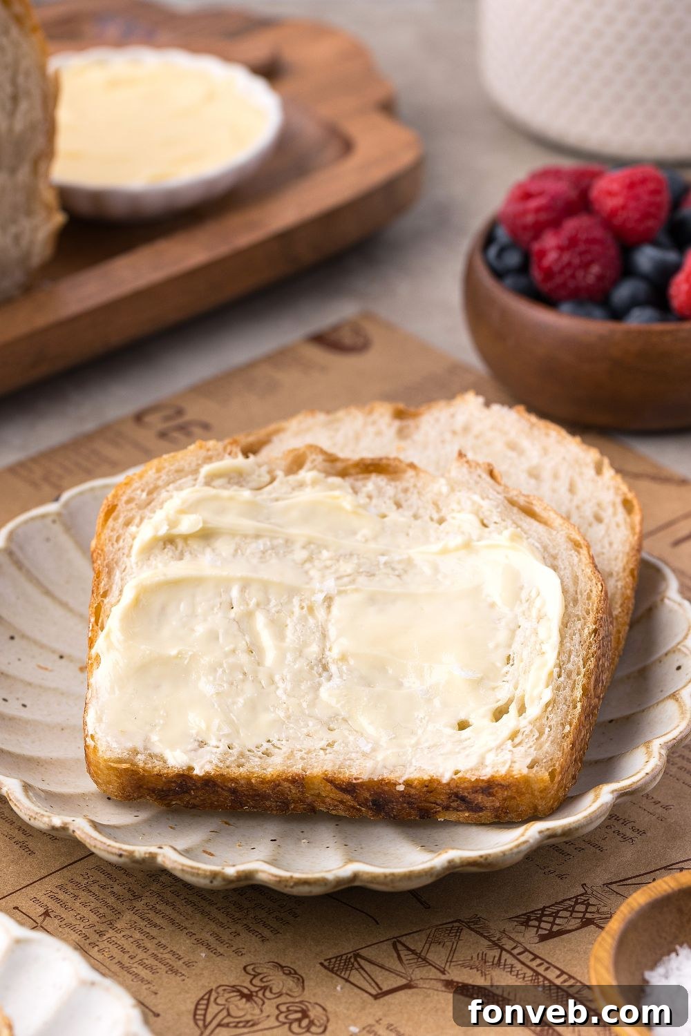 Effortless Homemade Sourdough Perfectly Crusty Always 23 Homemade Sourdough Bread sliced and buttered sitting on plate with a bowl of fruit behind it on table