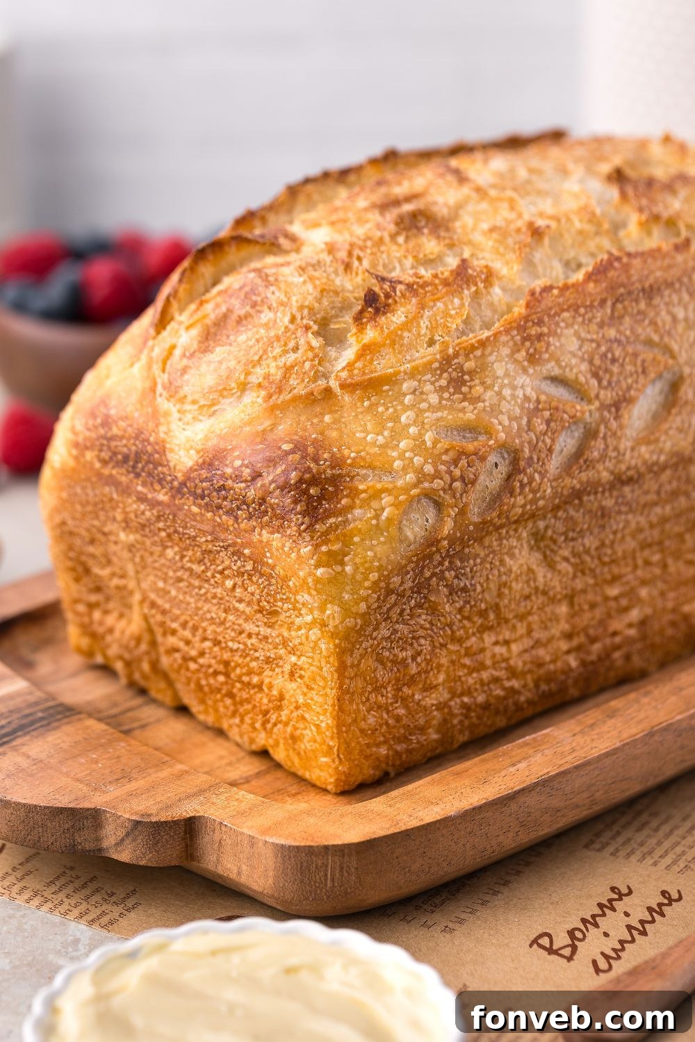 Effortless Homemade Sourdough Perfectly Crusty Always 4 Homemade Sourdough Bread sitting on a cutting board with berries in a bowl to the side of table