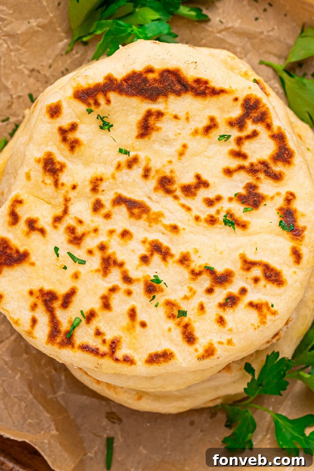 A stack of golden brown 3-Ingredient Flatbreads on a table, surrounded by scattered parsley