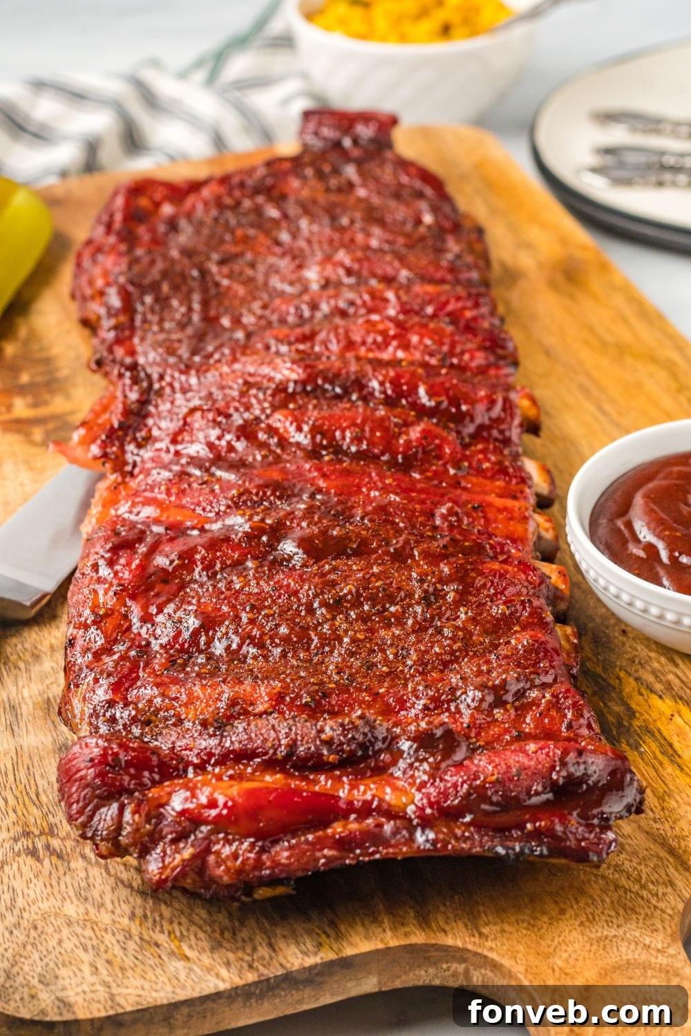 Grilled BBQ Baby Back Ribs on a wooden cutting board with more sauce in a bowl