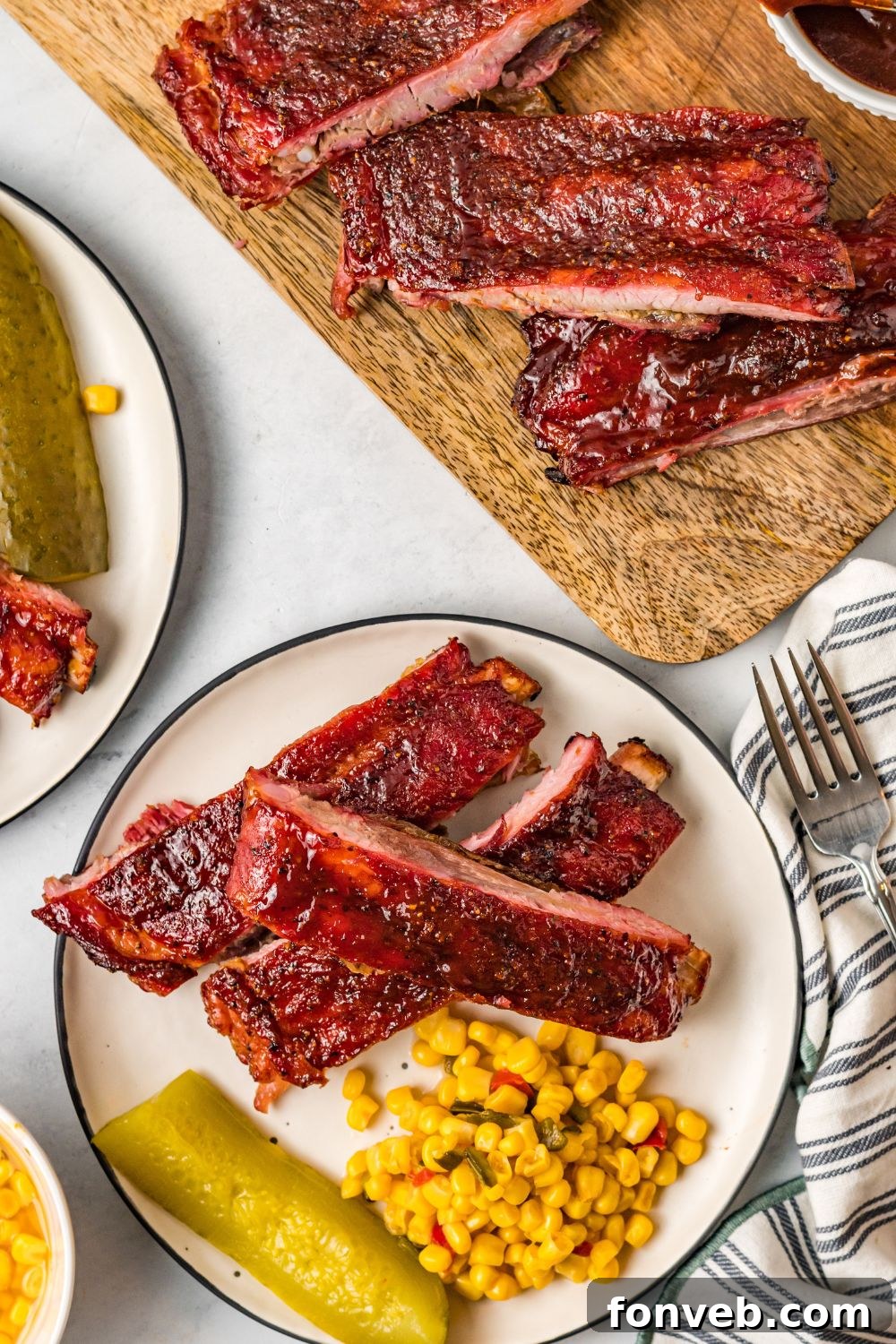 looking down at table with Grilled BBQ Baby Back Ribs on plates and a cutting board with corn and pickles on plates