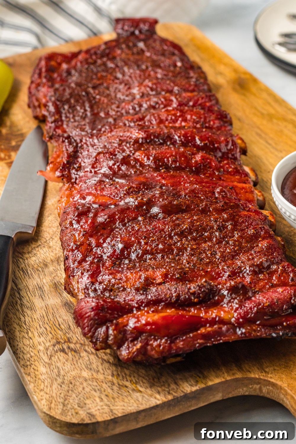 Grilled BBQ Baby Back Ribs on table with sharp knife to side and a bowl of bbq sauce