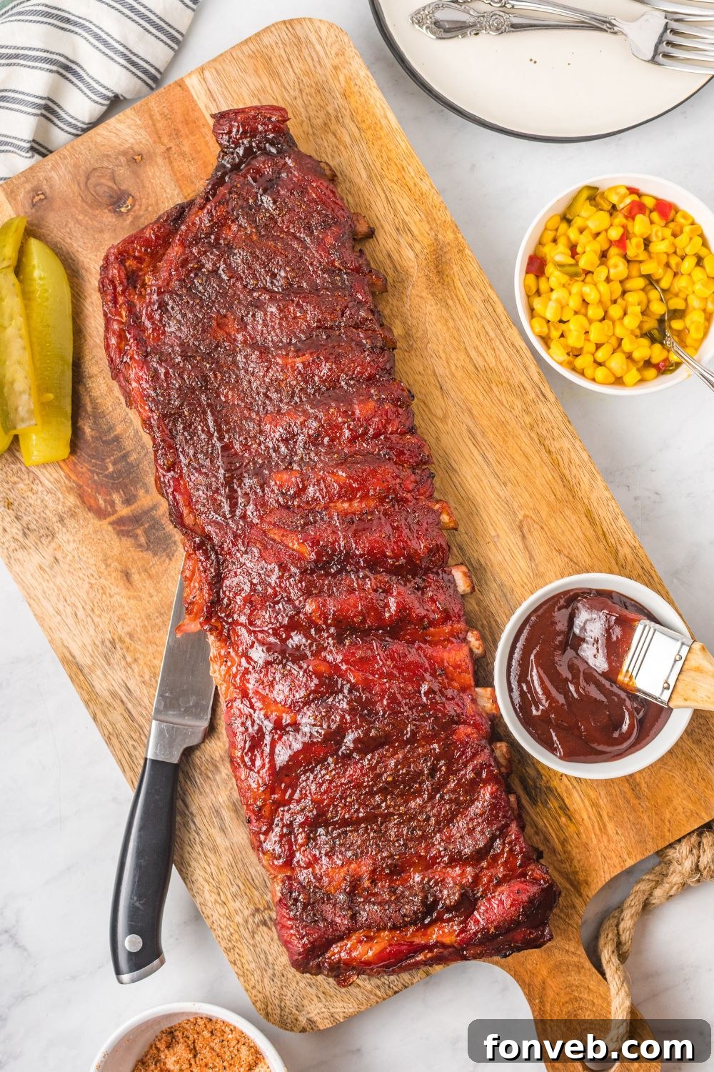 Grilled BBQ Baby Back Ribs on cutting board with sauce and corn to side in bowls