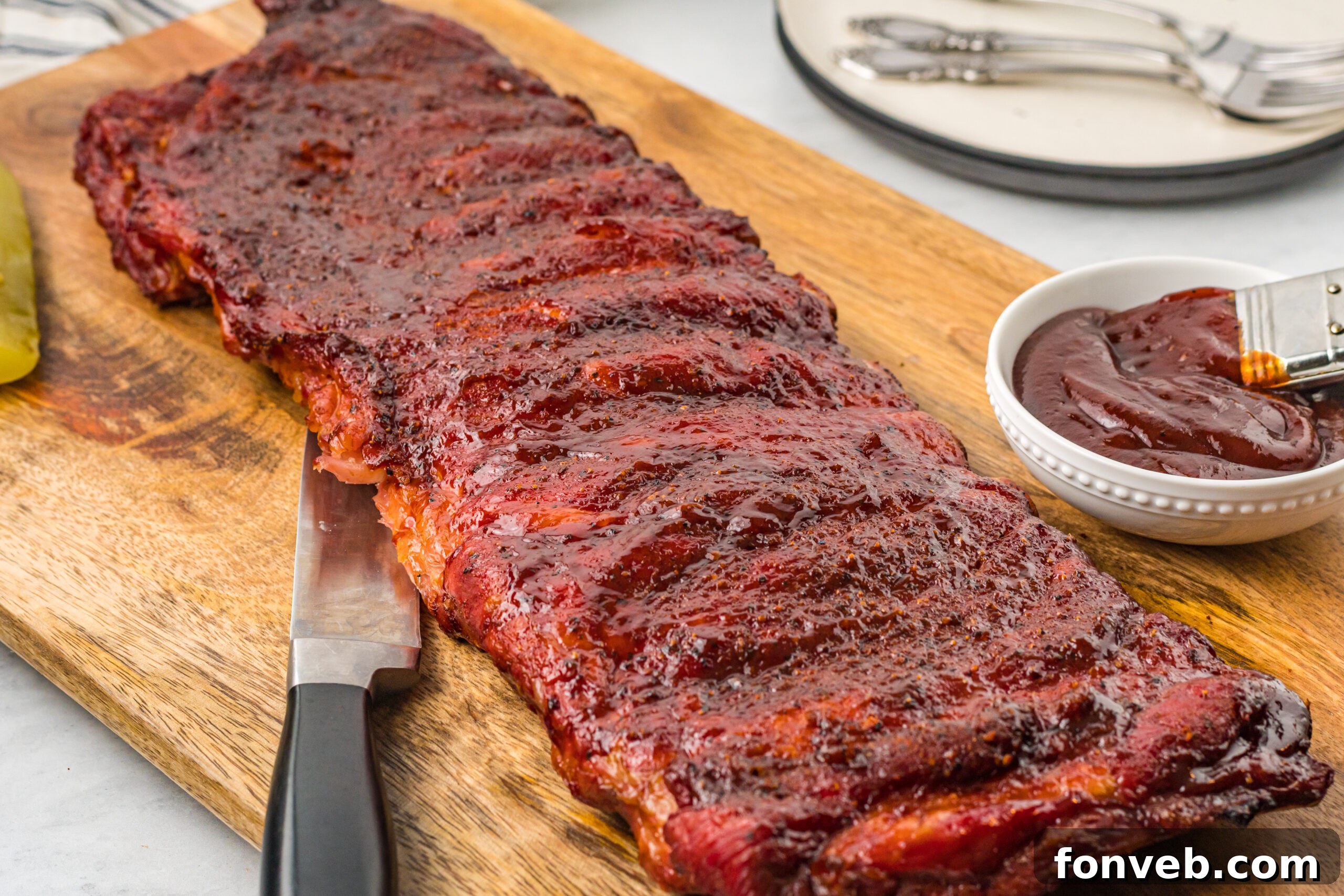 Grilled BBQ Baby Back Ribs on a wooden cutting board with more sauce in a bowl next to them
