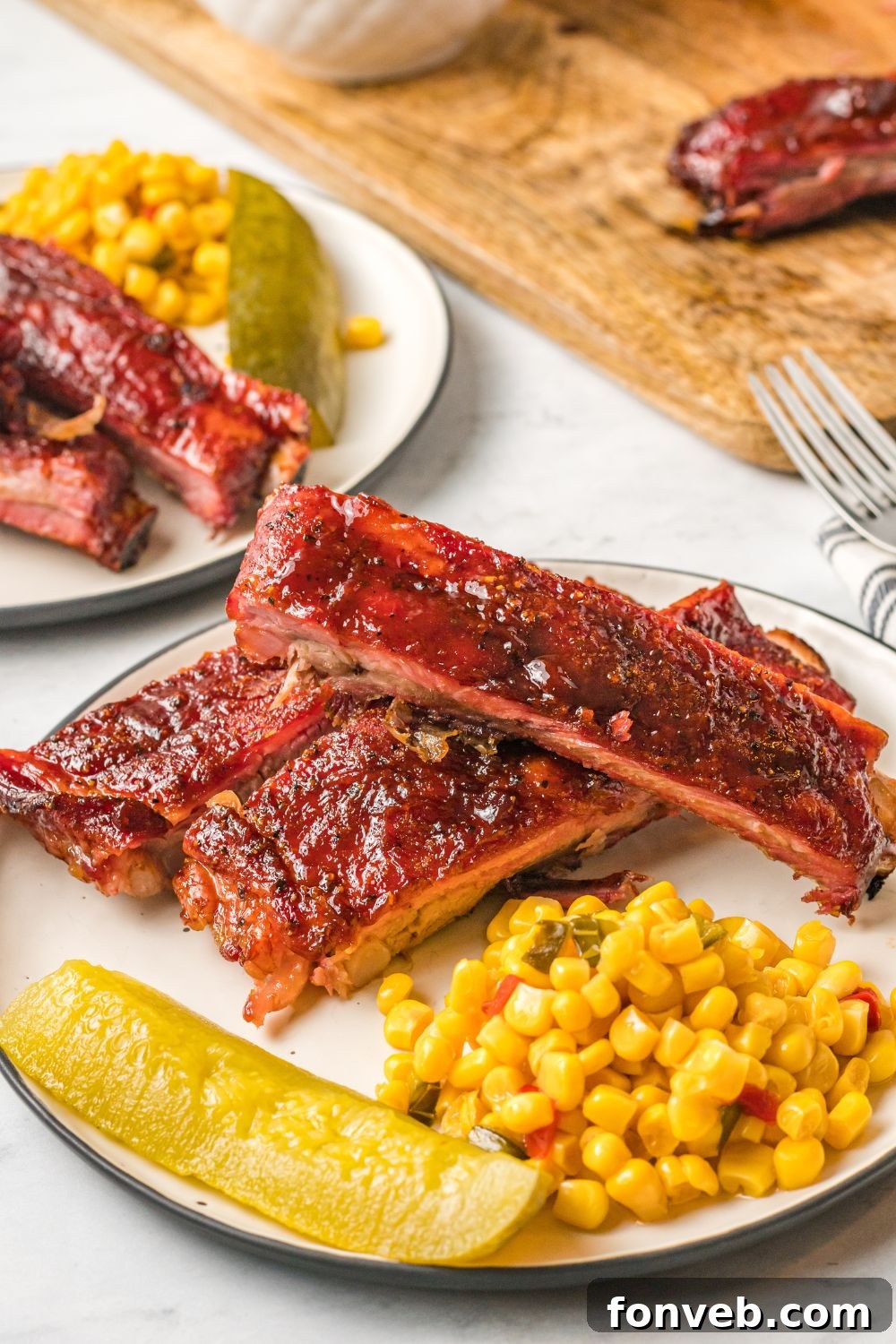 Grilled BBQ Baby Back Ribs on plate with corn and a pickle spear sitting on table