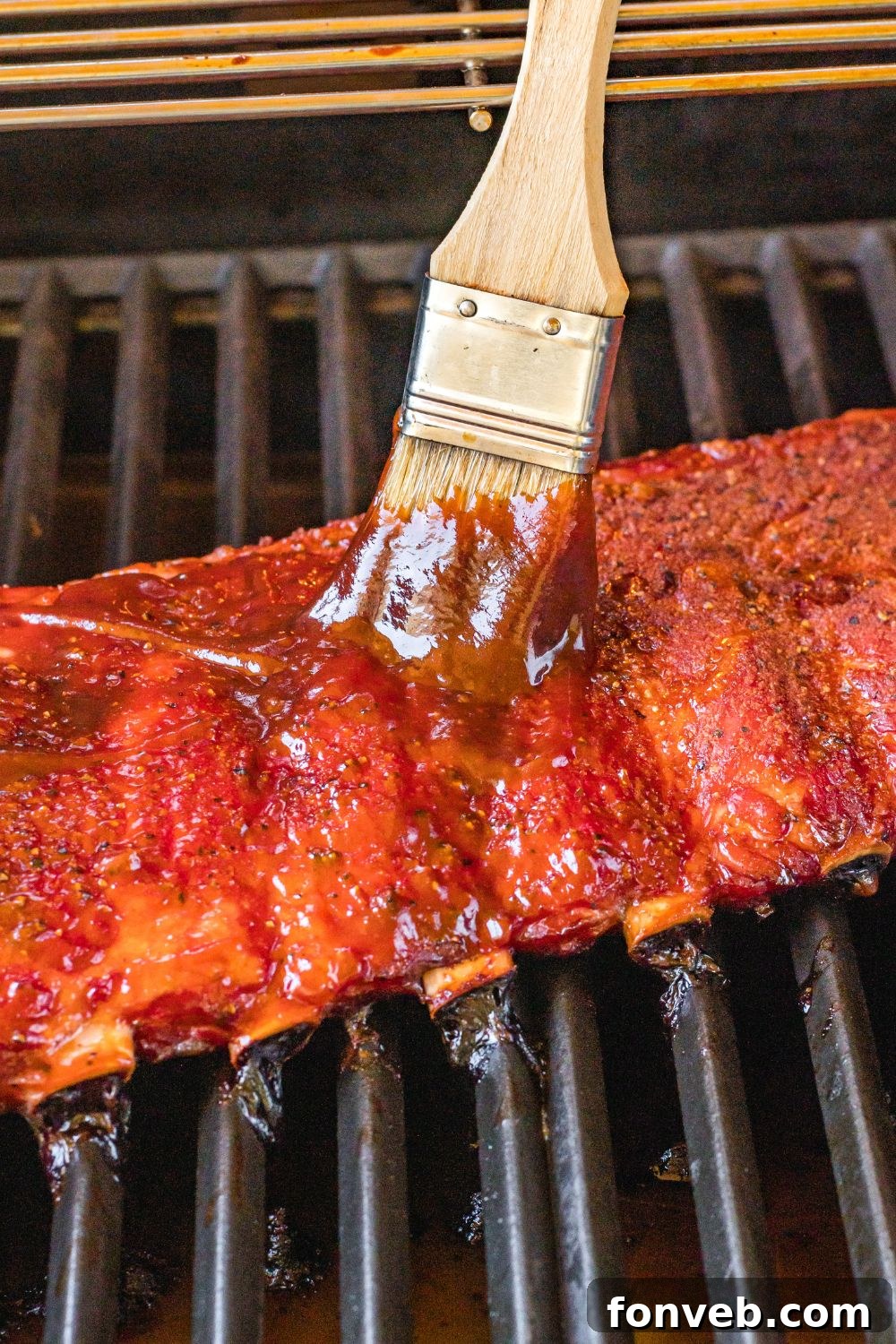 baby back ribs on grill being brushed with sauce