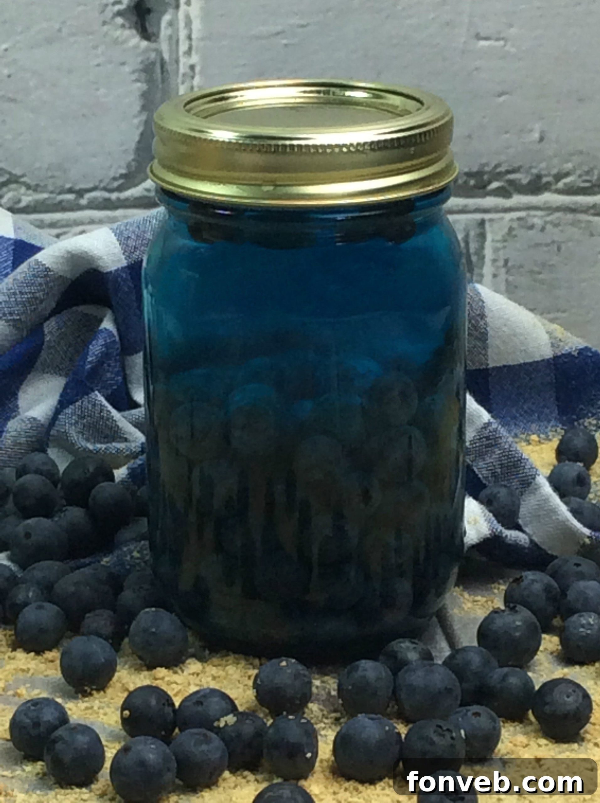 A hand holding a mason jar of Blueberry Cobbler Moonshine, showing its vibrant color