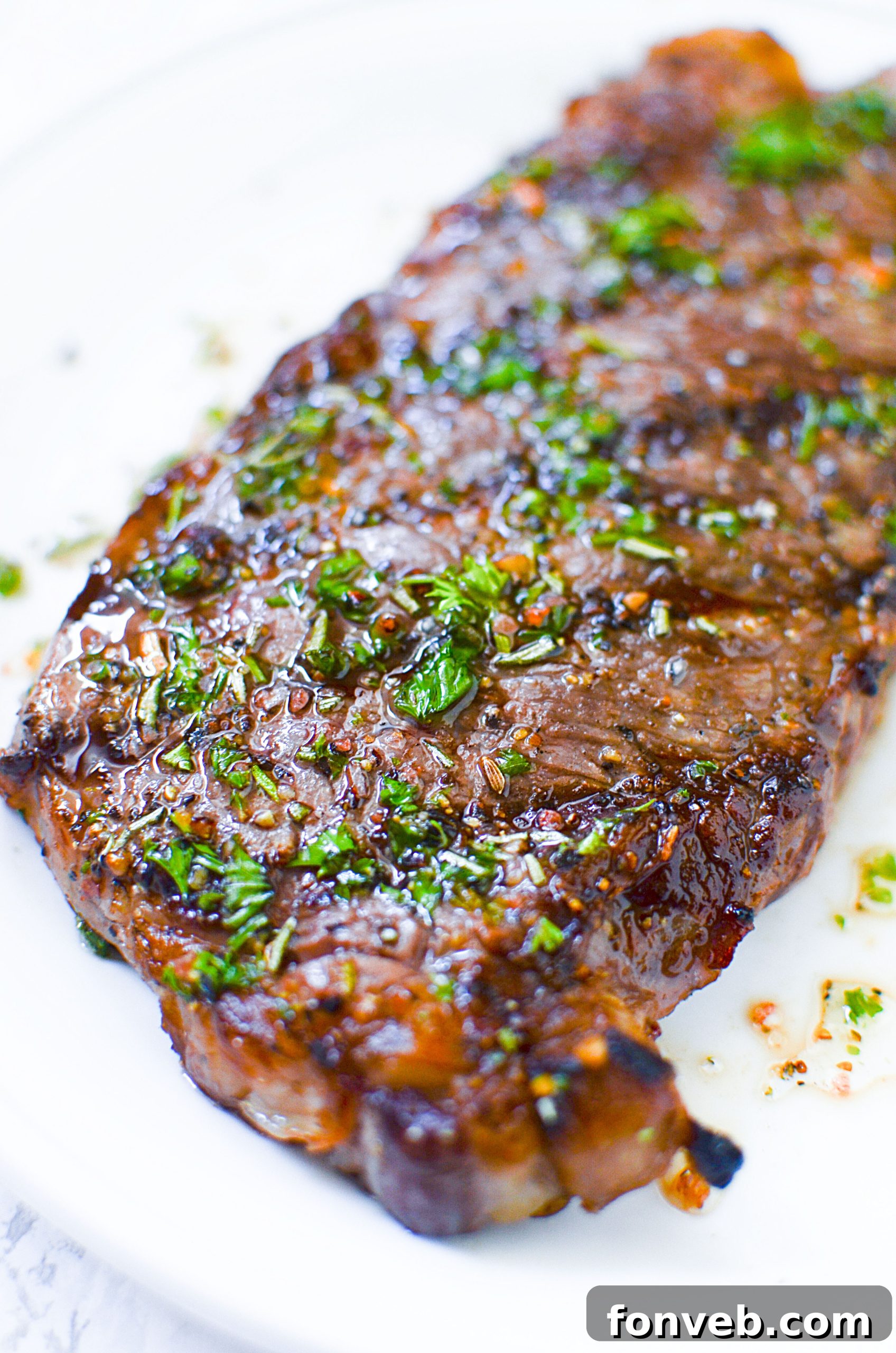 Close-up of a grilled steak garnished with fresh herbs, presented on a plate, ready to be served.