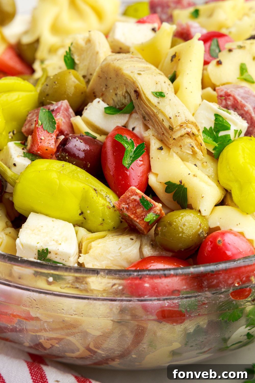 Antipasto Tortellini Pasta Salad in a bowl with close up of artichokes, peppers and more 