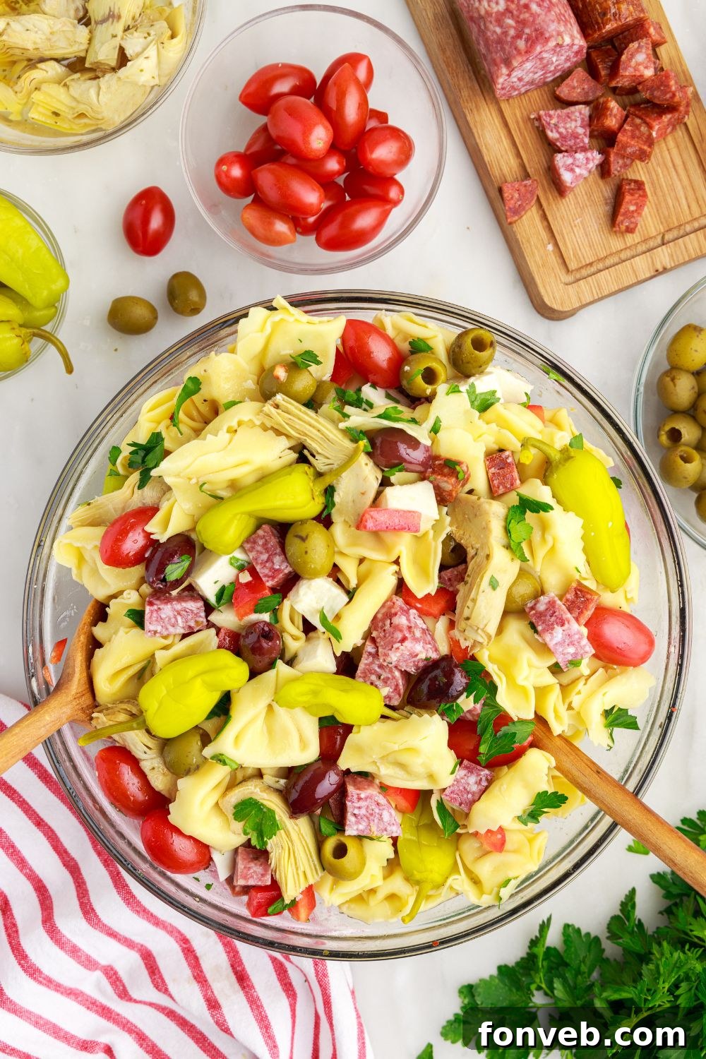 Antipasto Tortellini Pasta Salad in a bowl with peppers and tomatoes around the bowl of pasta 