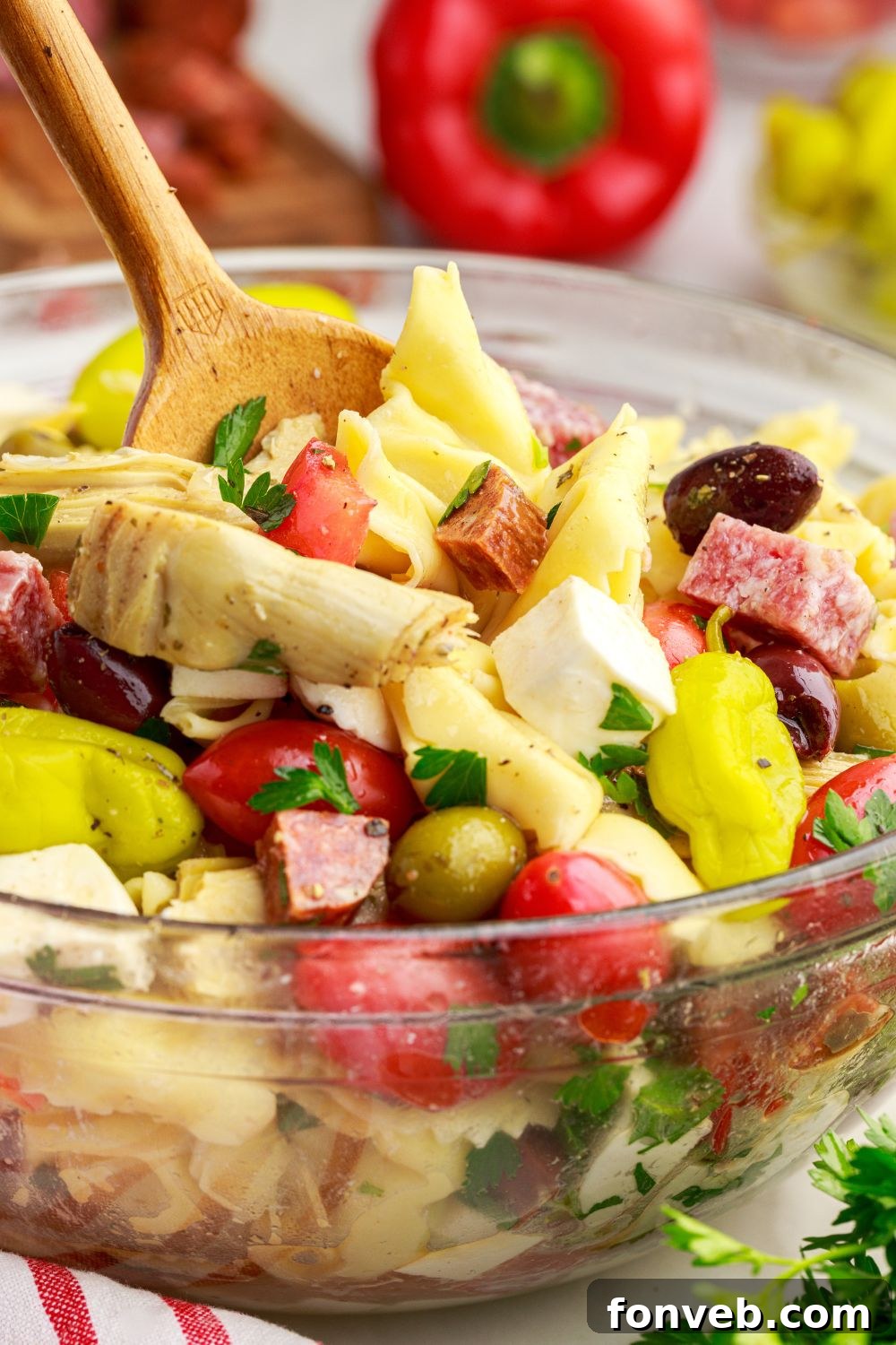 Antipasto Tortellini Pasta Salad in a glass bowl on table with a wooden spoon in bowl 