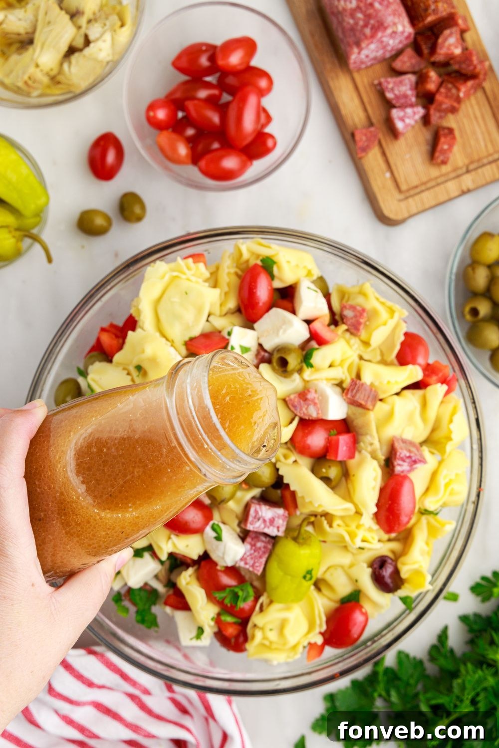 sauce pouring over Antipasto Tortellini Pasta Salad in a glass bowl