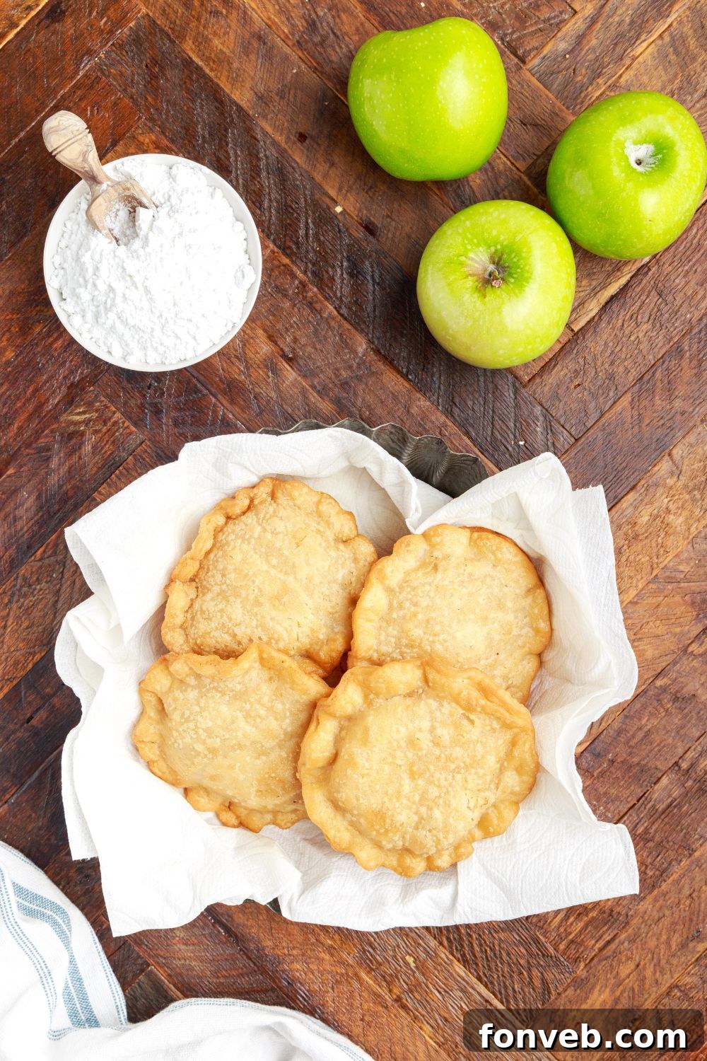 Golden Glazed Apple Hand Pies 16 Deep Fried Apple Hand Pies in a basket on table with powdered sugar to the side and green apples