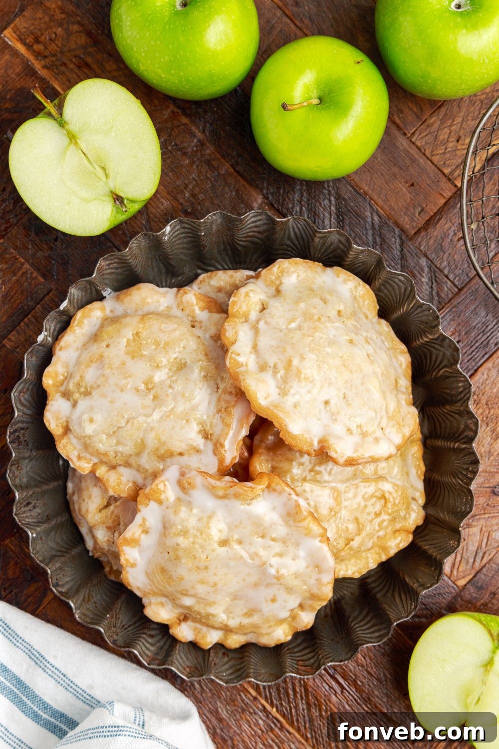 Golden Glazed Apple Hand Pies 18 Deep Fried Apple Hand Pies on a plate with a bunch of apples around it on table and one apple cut in half