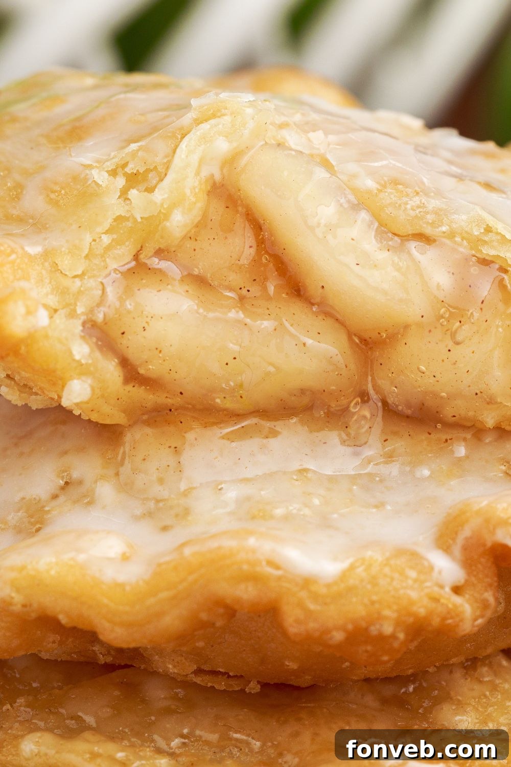 Golden Glazed Apple Hand Pies 19 Deep Fried Apple Hand Pies stacked on top of each other with one that has a bite taken out of it