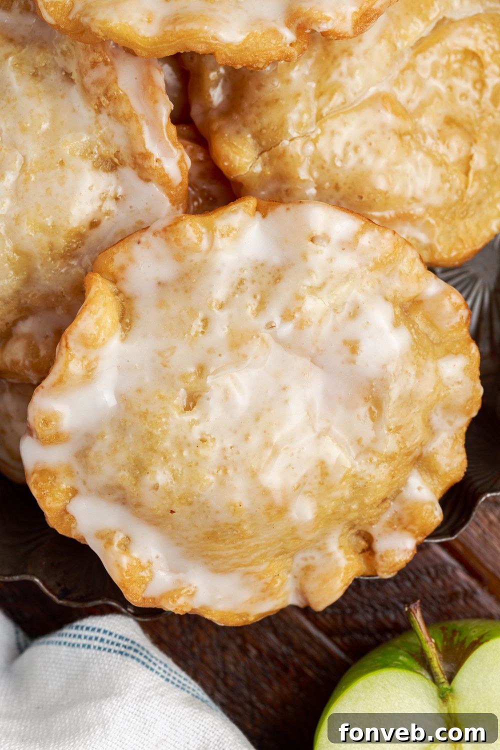 Golden Glazed Apple Hand Pies 4 Deep Fried Apple Hand Pies spread out on table with a half an apple to the side