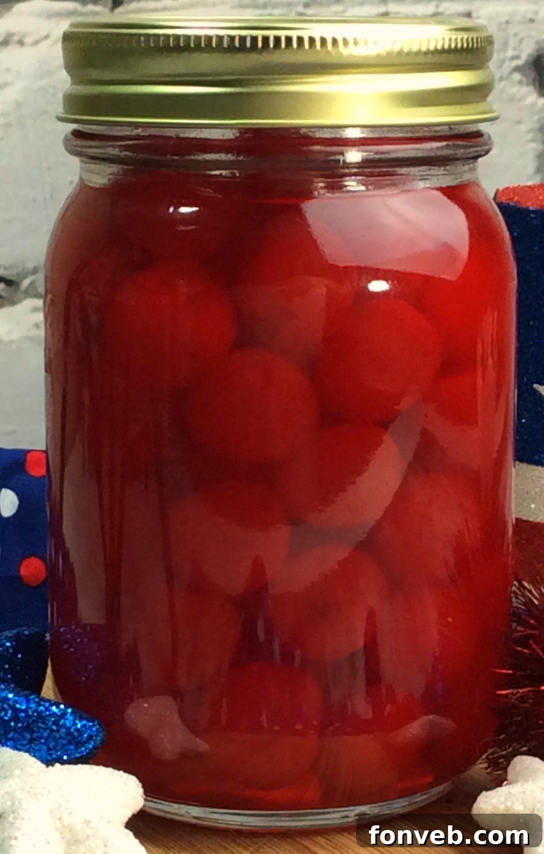 Close-up of a jar filled with vibrant red cherry moonshine, showcasing the whole cherries submerged in the liquid.