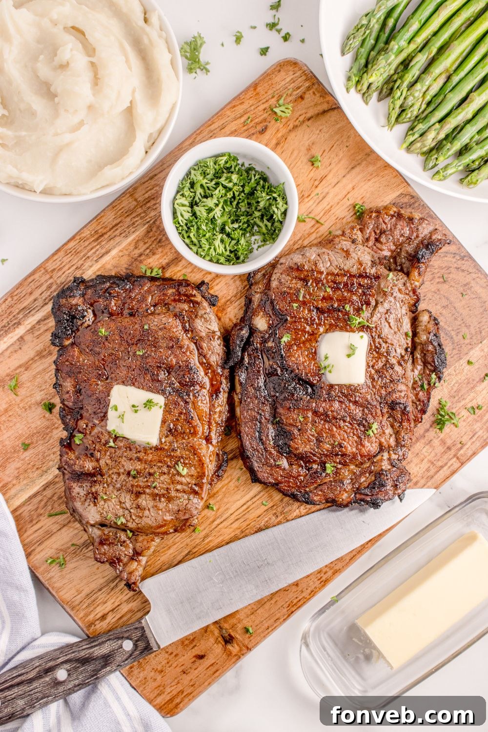 Grilled Ribeye Steaks on a cutting board with slabs of butter and bowl of parsley to the side 