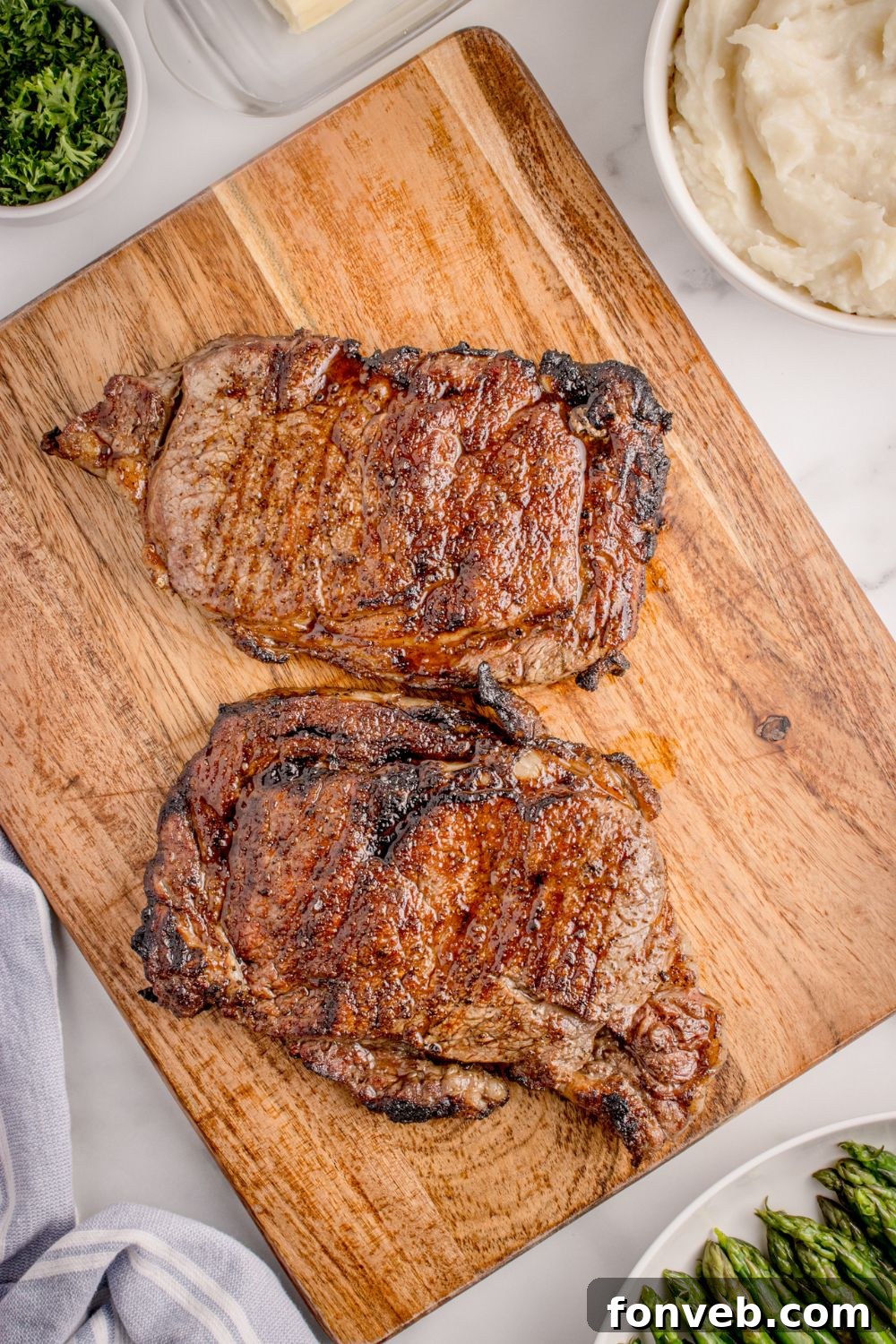 Grilled Ribeye Steaks on wooden cutting board sitting on table 