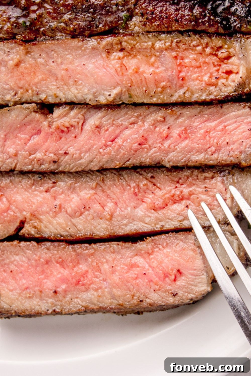 Grilled Ribeye Steak sliced into strips, with a close up of the redness and a fork to side 