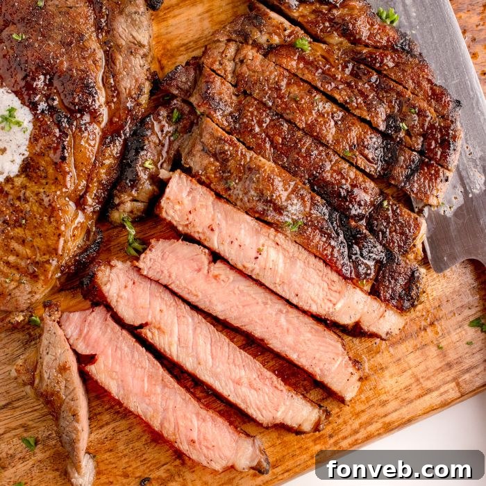Grilled Ribeye Steak sliced on cutting board with a whole steak to side 