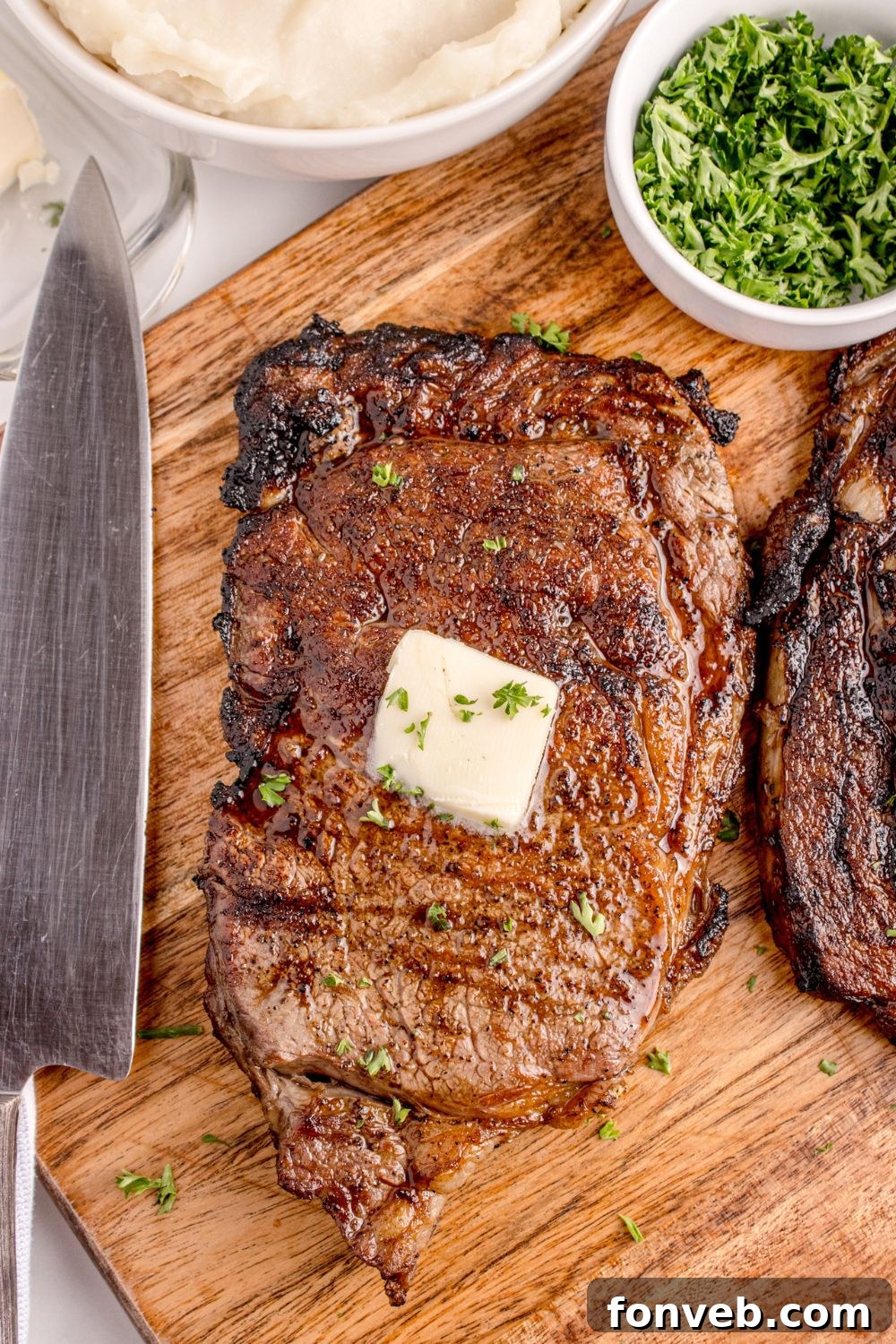 butter on top of Grilled Ribeye Steak on cutting board with knife sitting next to it on counter 