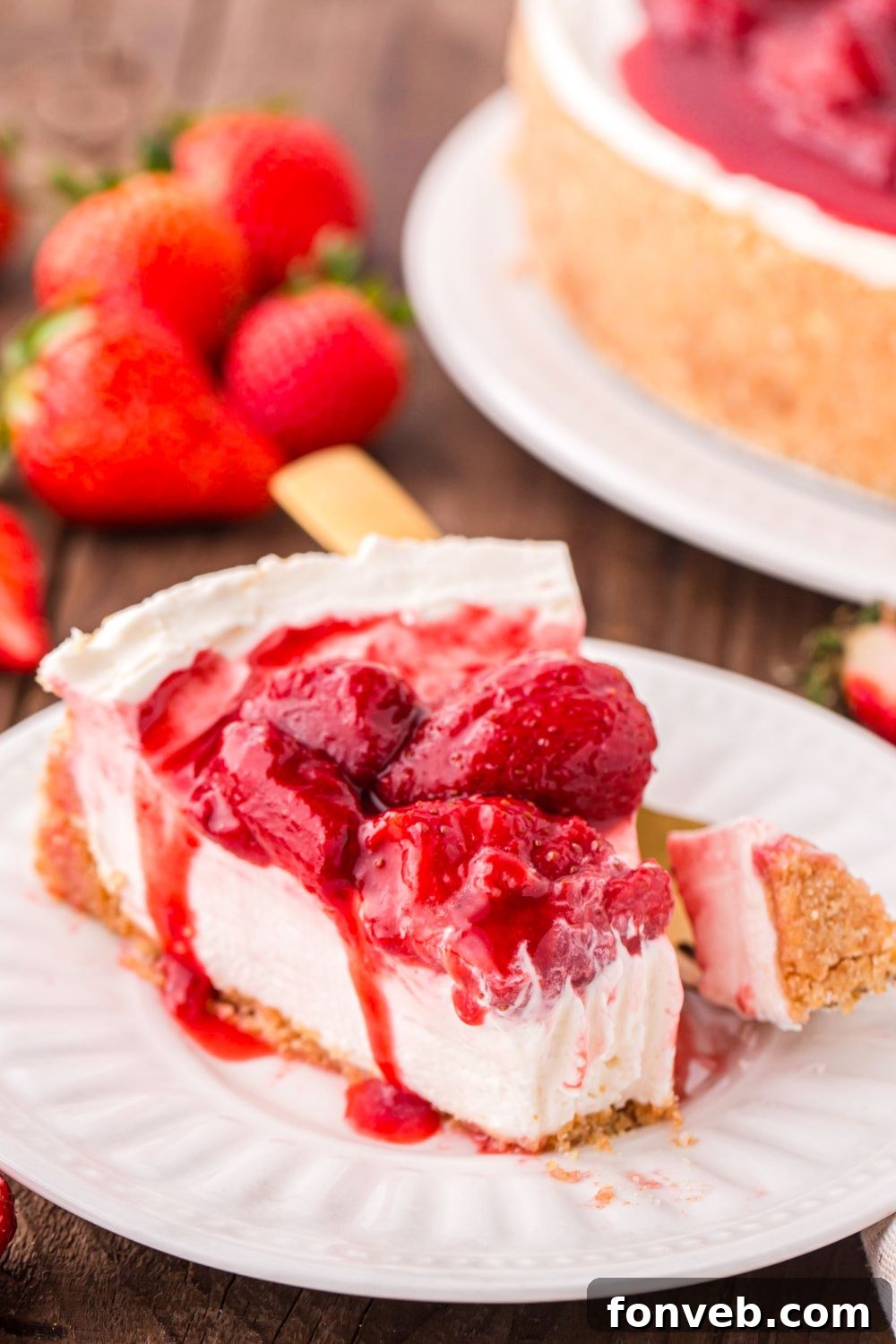 slice of No Bake Strawberry Cheesecake with a bite taken out of it sitting on plate with fresh strawberries in the background 