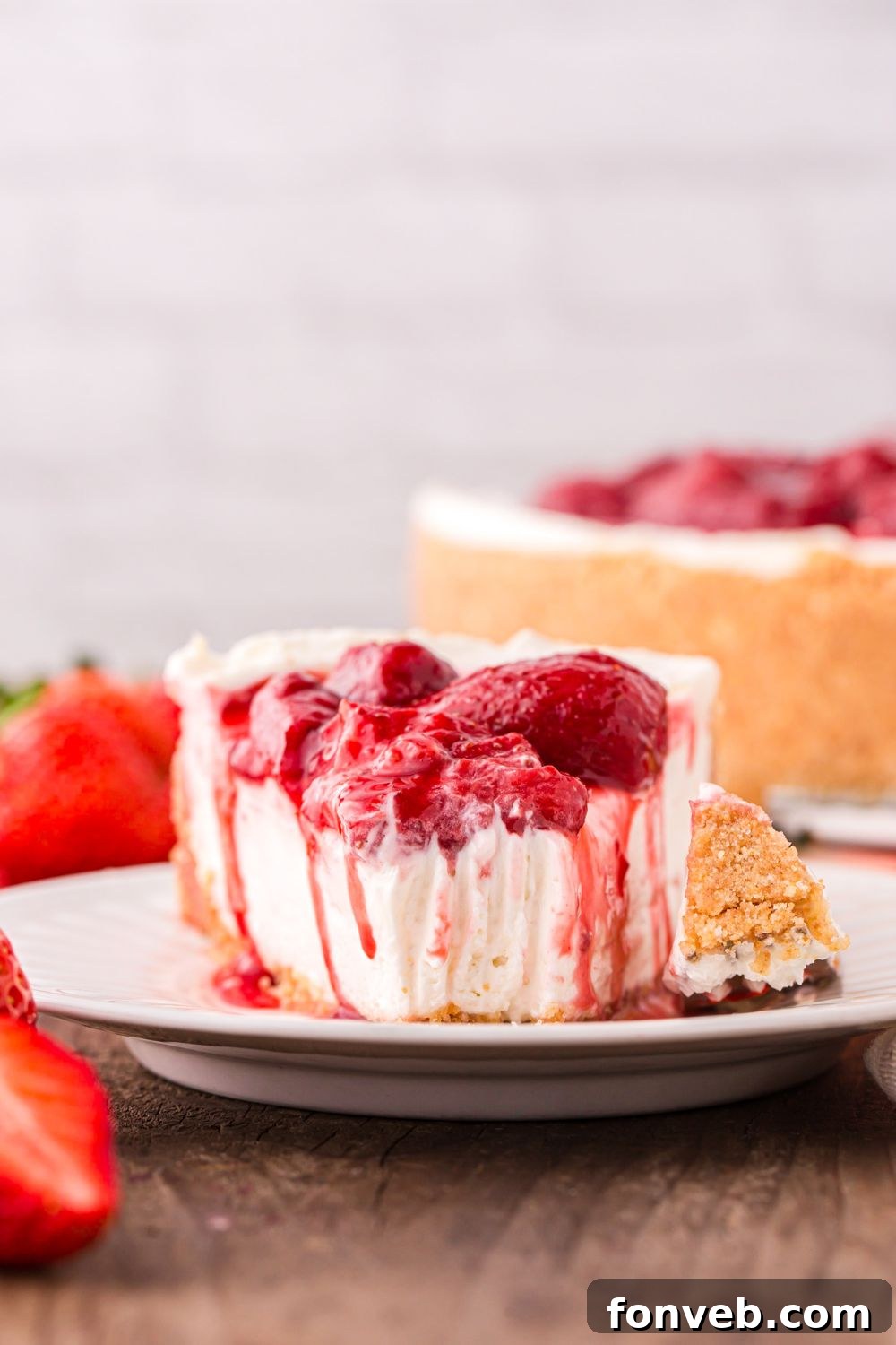 No Bake Strawberry Cheesecake on plate with a bite cut out and the rest of cheesecake behind it on table 