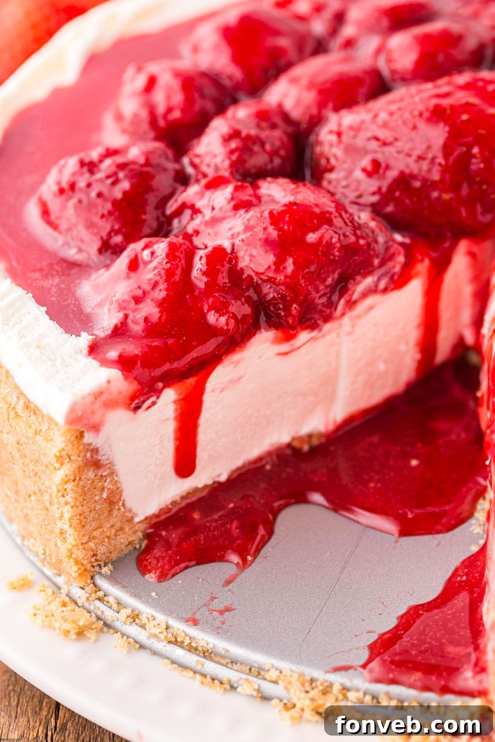 view of No Bake Strawberry Cheesecake on table with sauce dripping down on cheesecake 