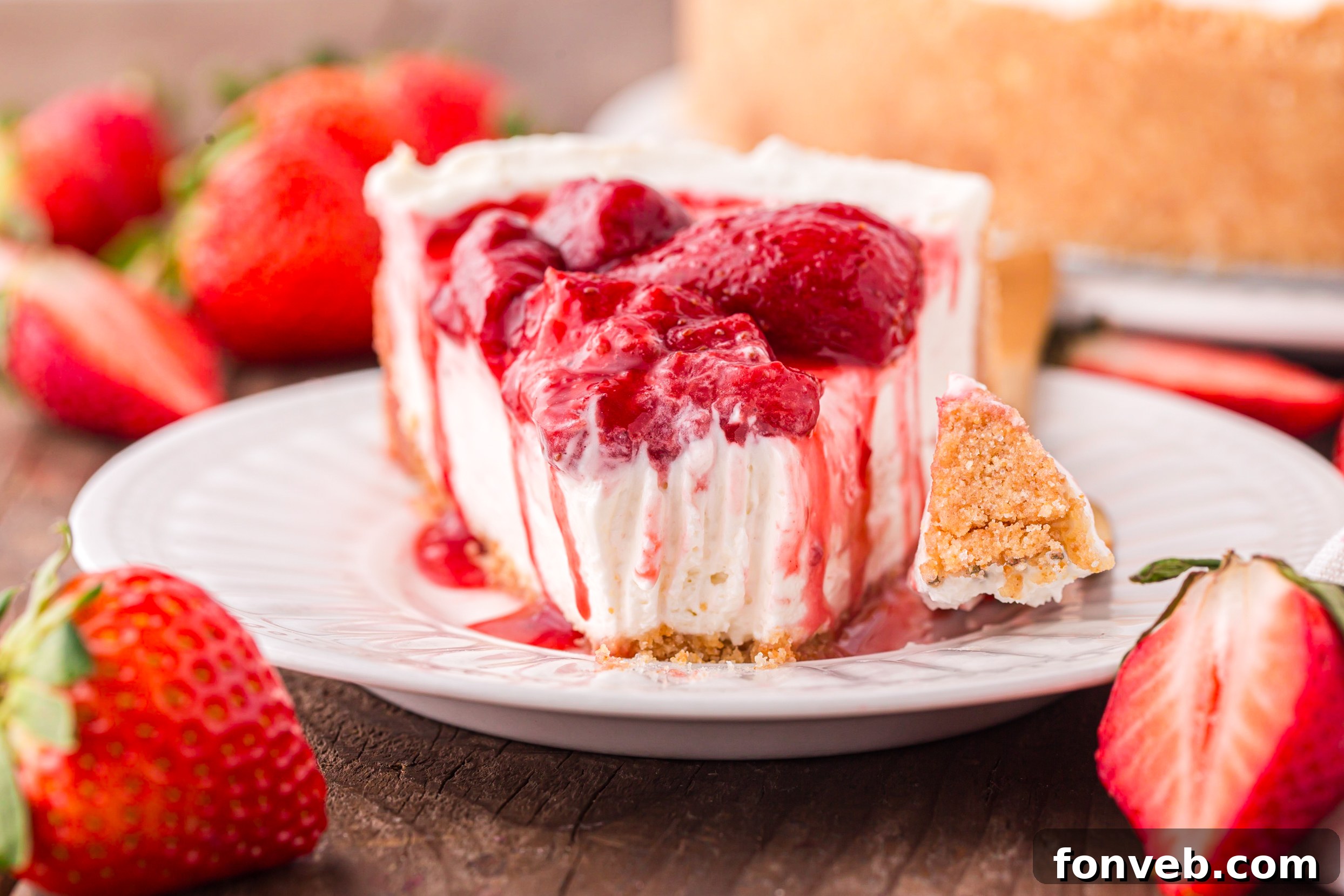 No Bake Strawberry Cheesecake up close on a white plate, topped with juicy strawberries with a bite missing 