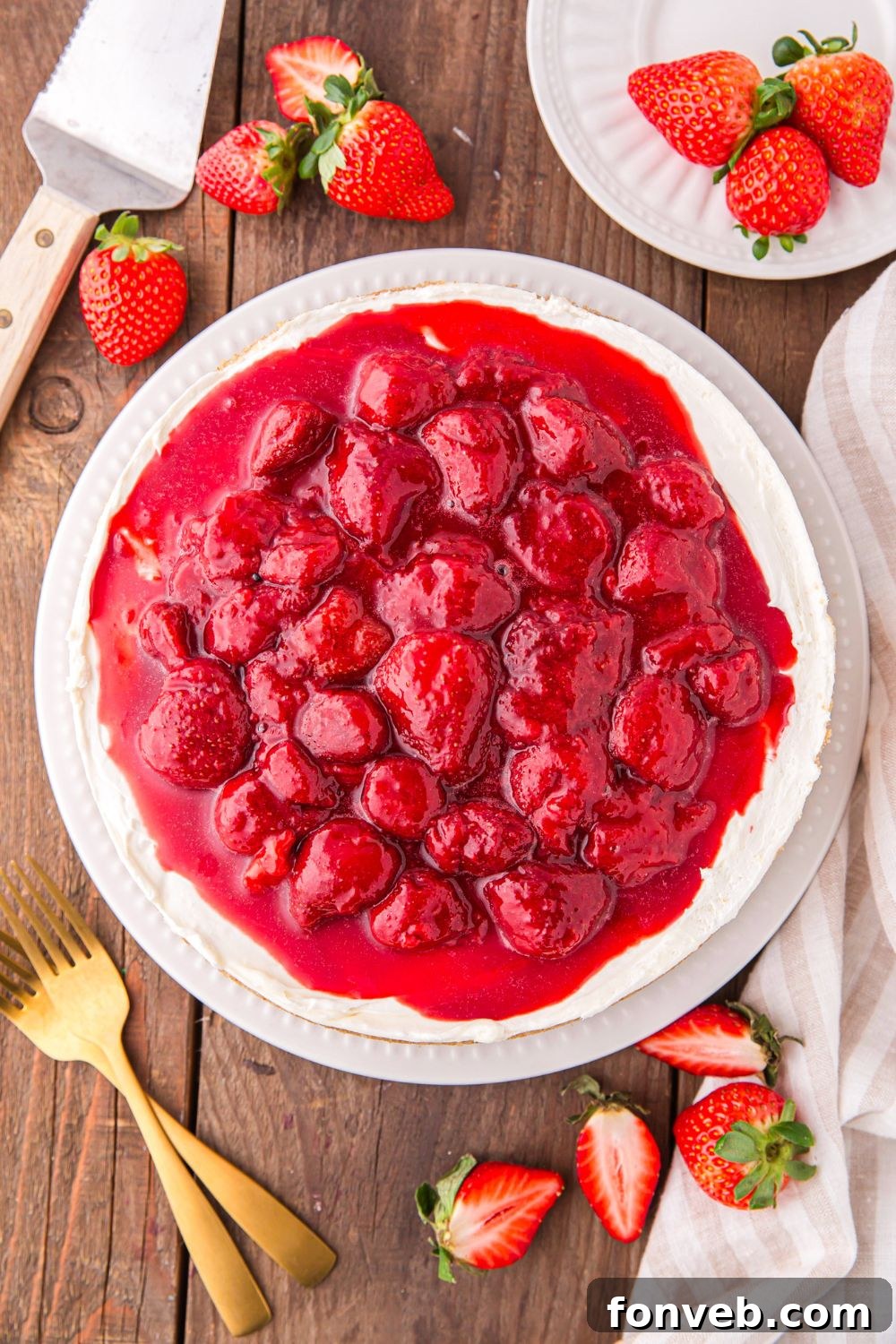 No Bake Strawberry Cheesecake sitting on table with fresh strawberries around it, forks, and plates 