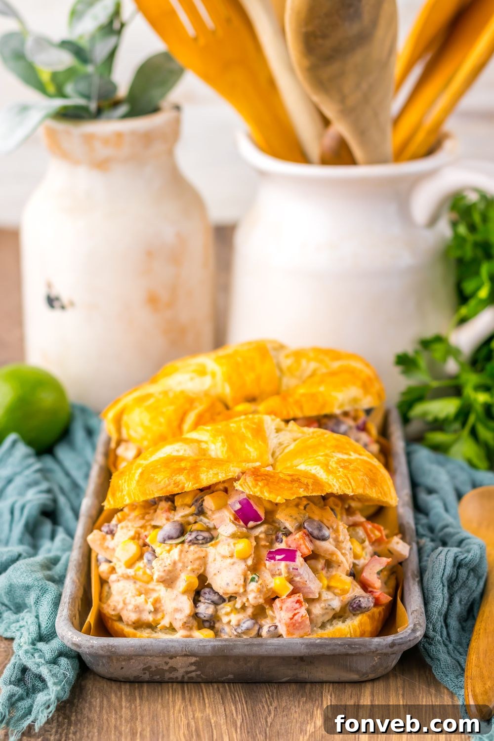 Creamy Taco Chicken Salad on croissants on table in tray with wooden spoons behind it on table 