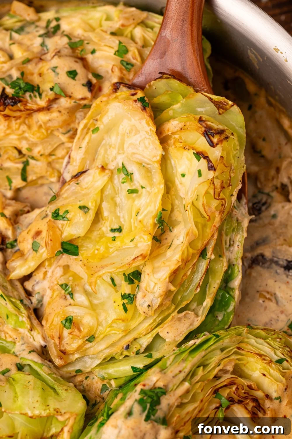 Keto Creamy Garlic Parmesan Cabbage Skillet 11 Creamy Garlic Parmesan Cabbage in a skillet, with one wedge being lifted by a spoon