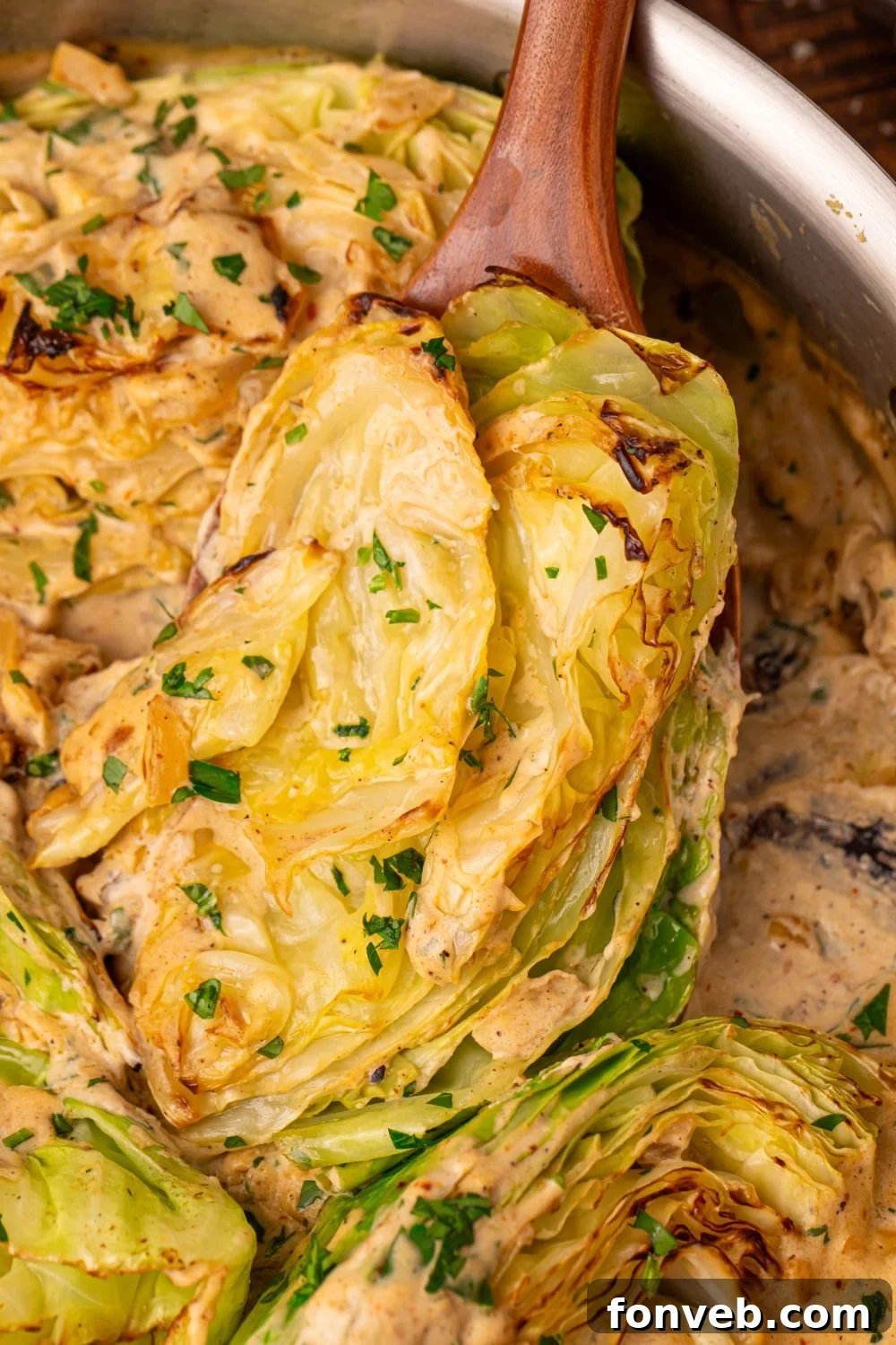 Keto Creamy Garlic Parmesan Cabbage Skillet 16 Creamy Garlic Parmesan Cabbage in a skillet, being lifted out with a wooden spoon