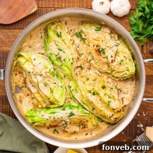 Creamy Garlic Parmesan Cabbage in a skillet on table with parsley and garlic beside it on table