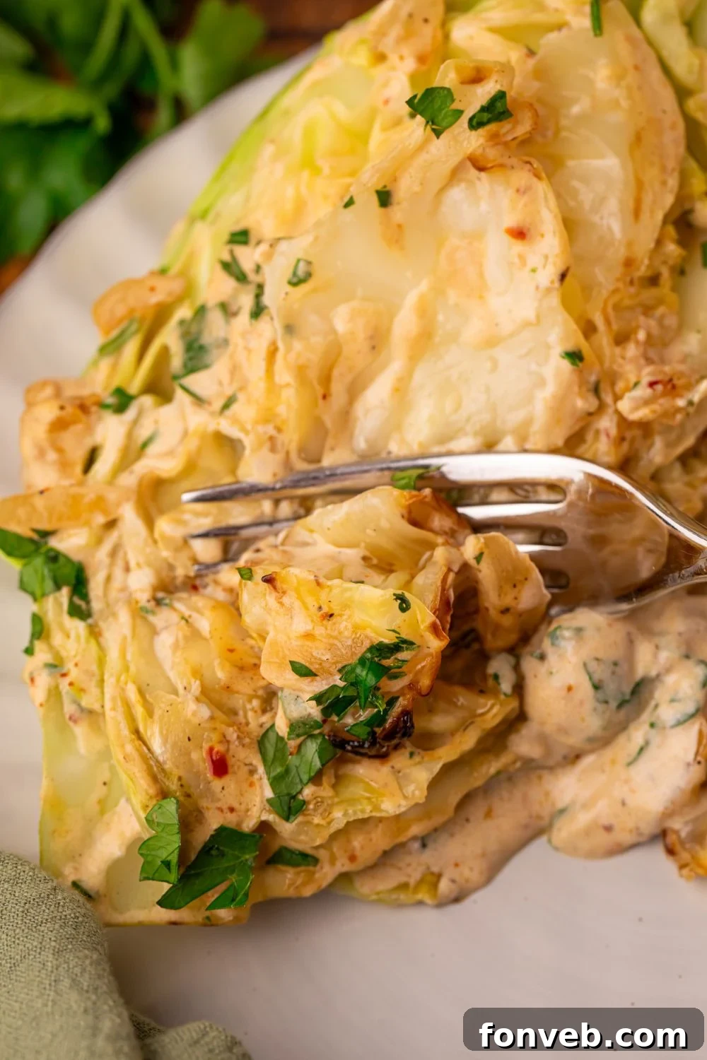 Keto Creamy Garlic Parmesan Cabbage Skillet 6 Creamy Garlic Parmesan Cabbage on a plate with a fork cutting into a wedge