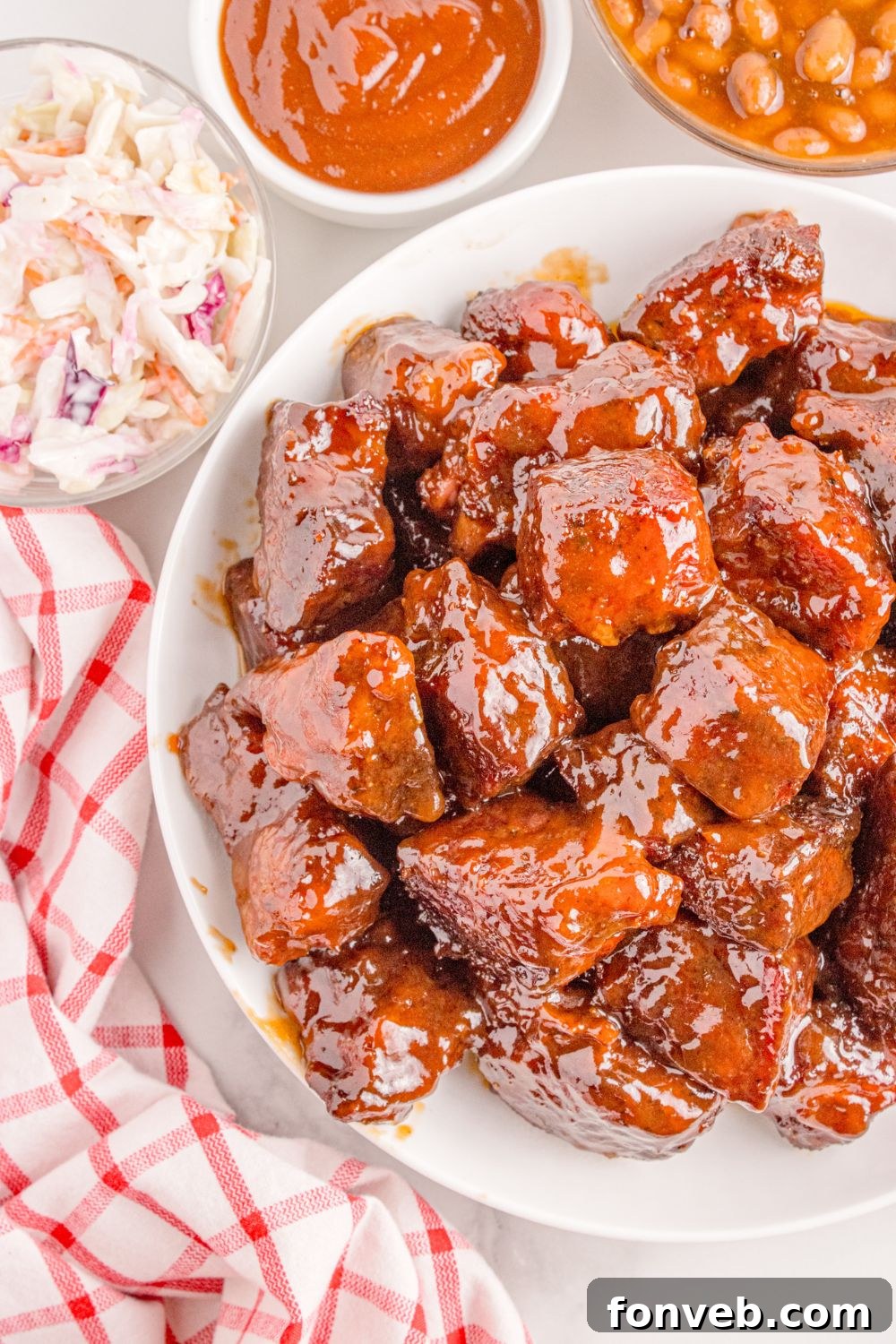 Chuck Roast Burnt Ends are elegantly arranged on a plate, surrounded by complementary side dishes including bowls of savory BBQ sauce, creamy coleslaw, and hearty baked beans, creating a complete and inviting meal.