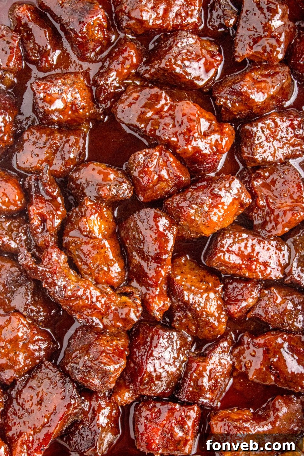 An overhead shot captures the delicious Chuck Roast Burnt Ends simmering in a foil pan on a table, their sticky glaze and tender texture ready to be savored.