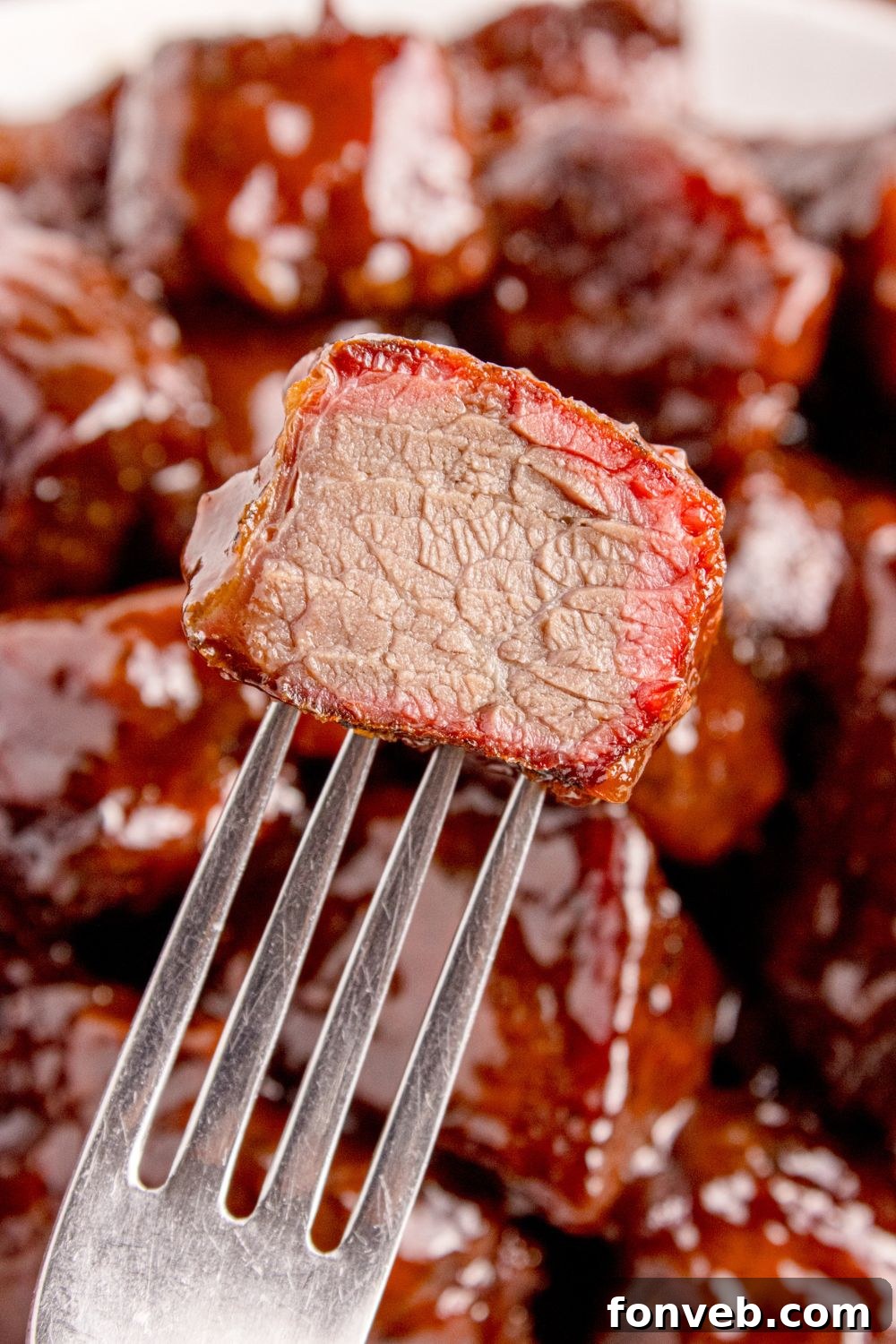 A single, perfectly cooked Chuck Roast Burnt End, cut in half, reveals its tender, juicy interior and beautiful bark, impaled on a fork, inviting a taste.