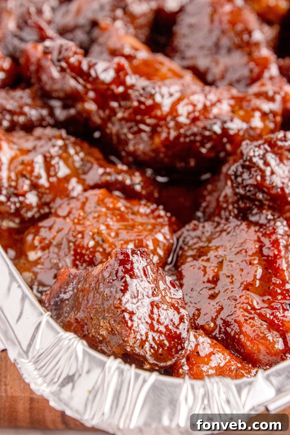A close-up view of Chuck Roast Burnt Ends simmering in a pan on a table, their rich, sticky glaze sparkling and their tender texture clearly visible.