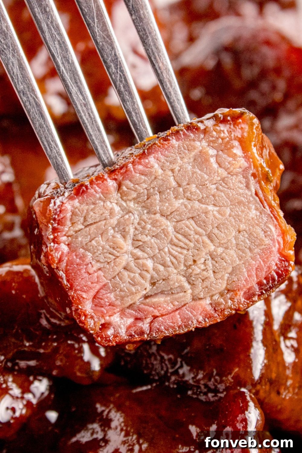 A fork lifts a piece of Chuck Roast Burnt End, clearly showing where a bite has been taken out, revealing the succulent, smoke-ringed meat within.