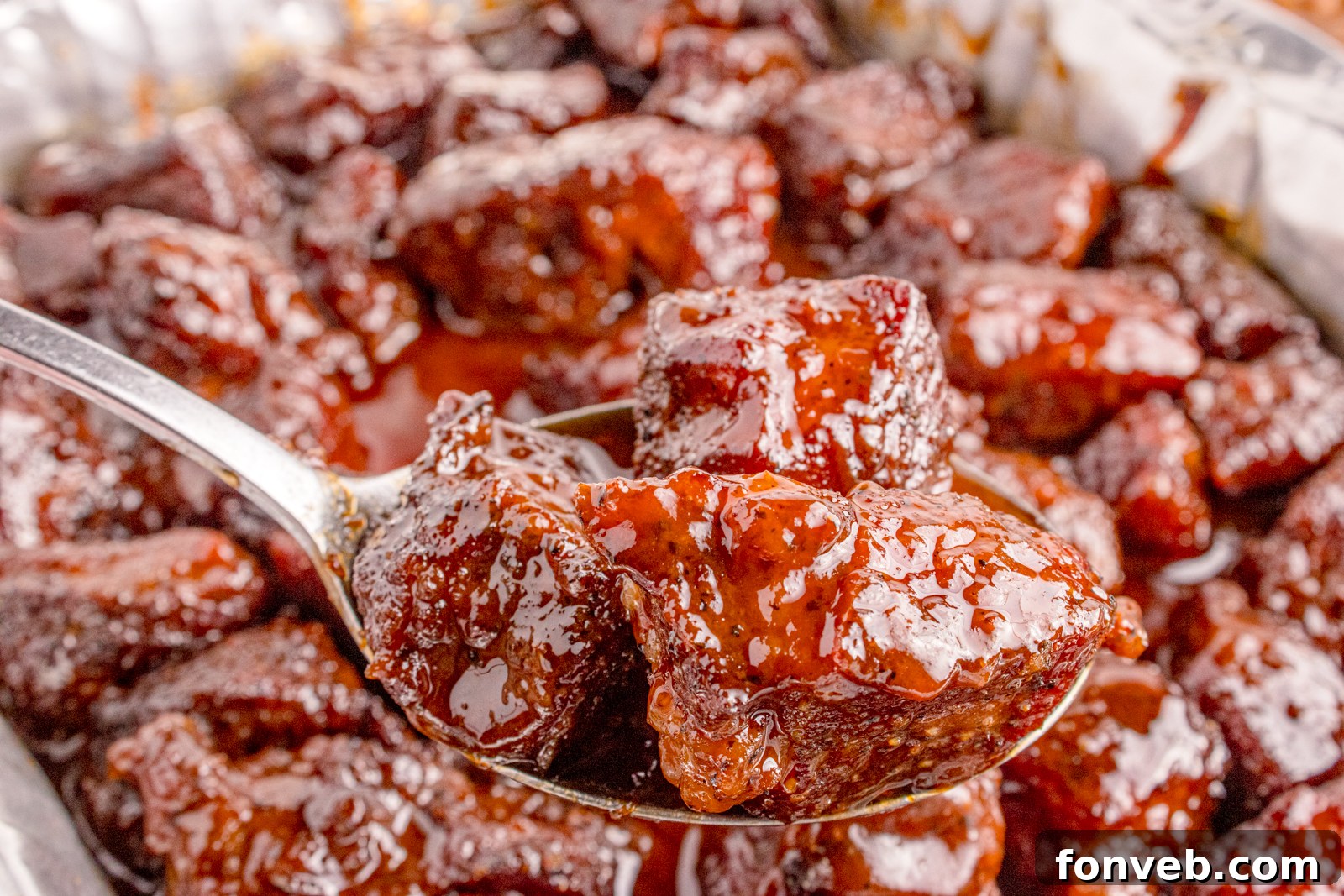 An inviting, close-up shot of Chuck Roast Burnt Ends nestled in a spoon, glistening with their rich, sticky glaze, ready to be enjoyed.