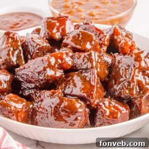 A generous bowl of smoky Chuck Roast Burnt Ends, glistening with rich BBQ sauce, sits on a rustic table. In the soft-focus background, a small dish of creamy beans and a bottle of barbecue sauce complete the appetizing scene.