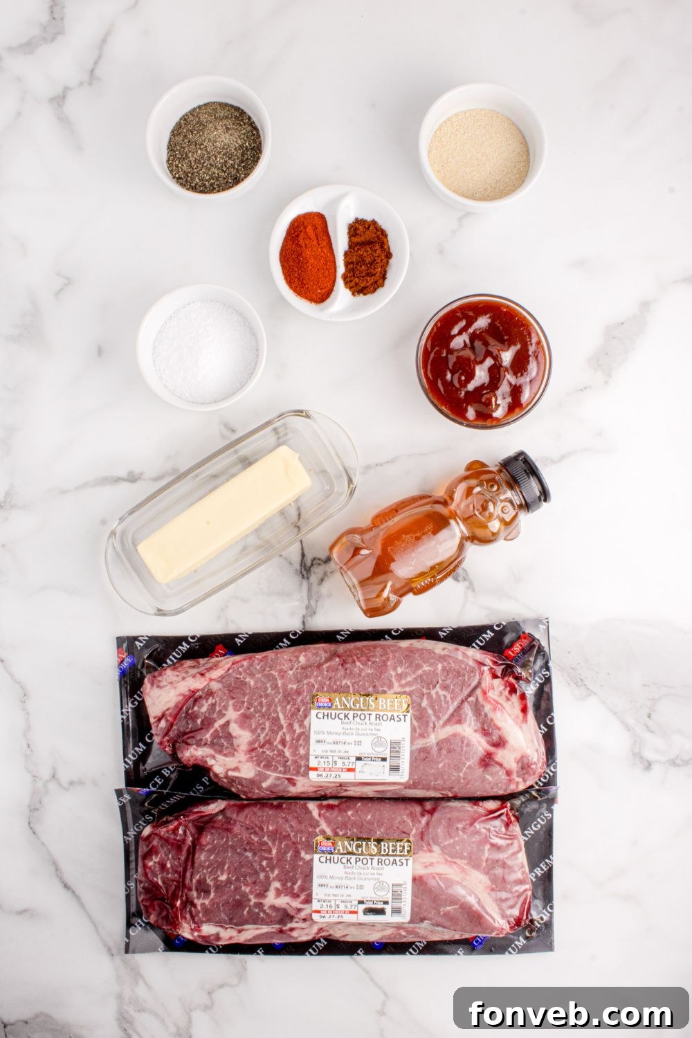 All the essential ingredients for making Chuck Roast Burnt Ends are artfully arranged on a rustic table, including a raw chuck roast, various spices, butter, honey, and barbecue sauce, ready for preparation.